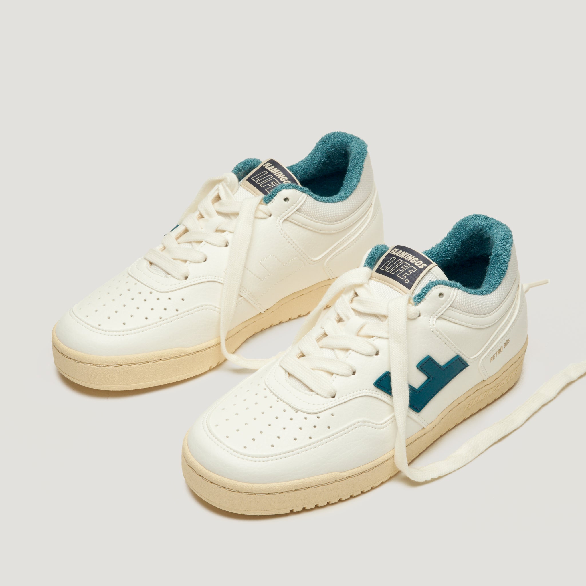 Weiße Sneaker mit beiger Sohle und blauen Akzenten, auf einem hellen Hintergrund stehend.