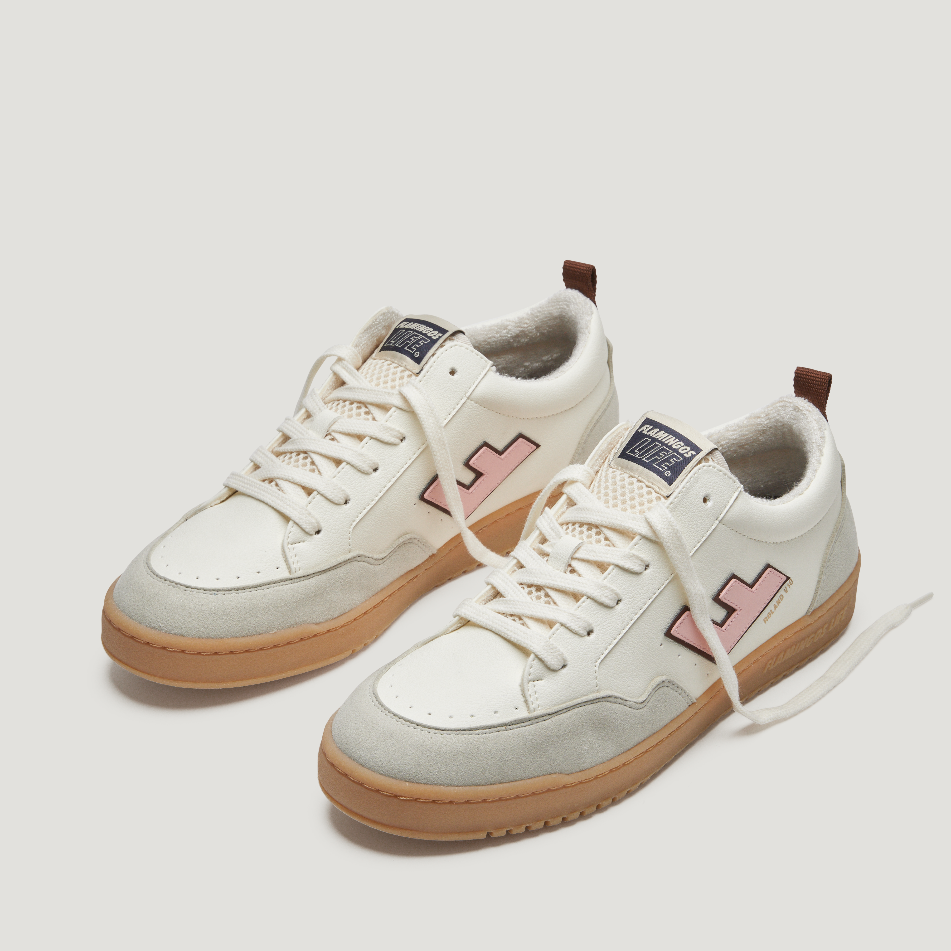 Weiße Sneaker mit rosa Details, beiger Sohle und braunem Ferseneinsatz auf weißem Hintergrund.