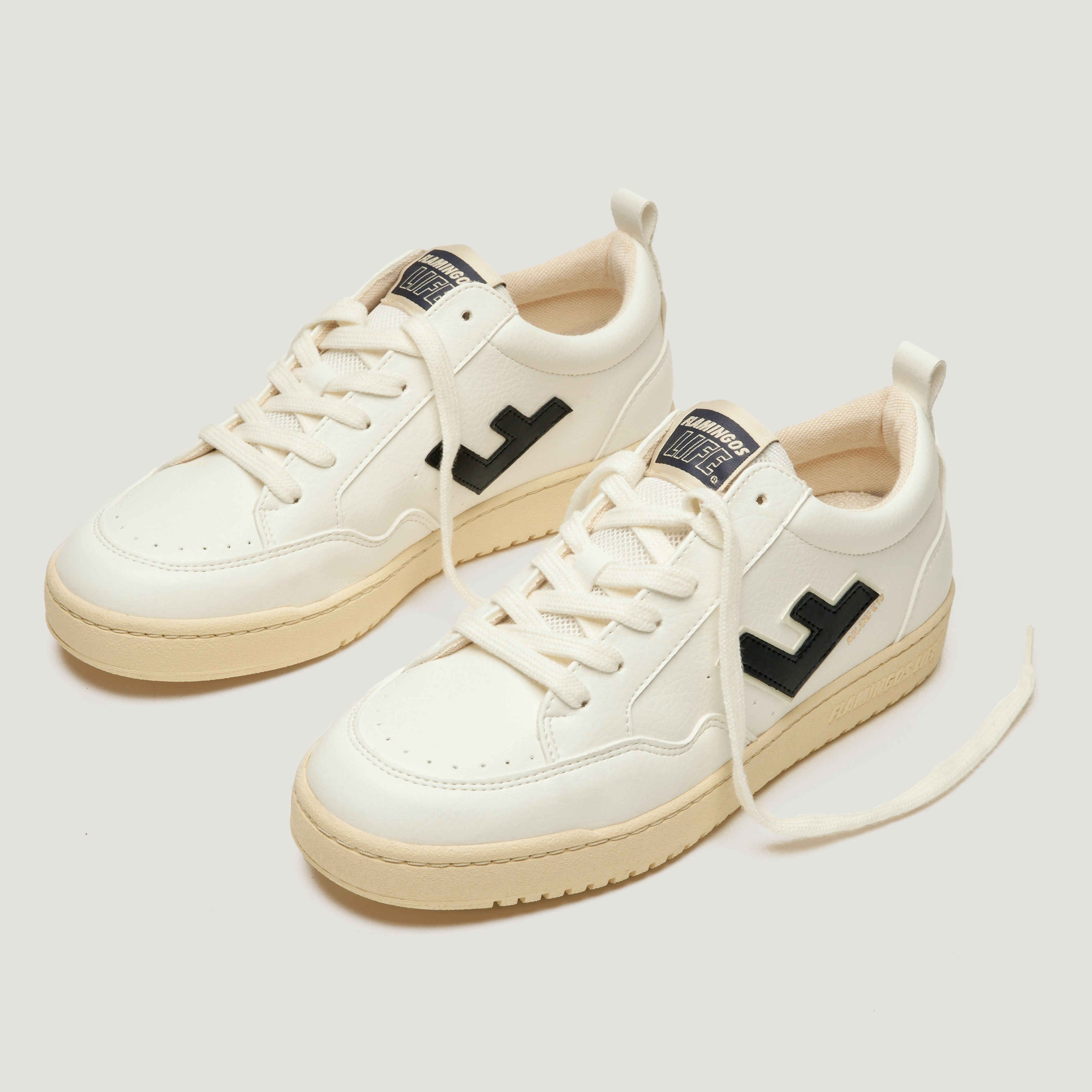 Weiße Sneaker mit schwarzem Logo und beigen Sohlen, auf hellem Hintergrund.