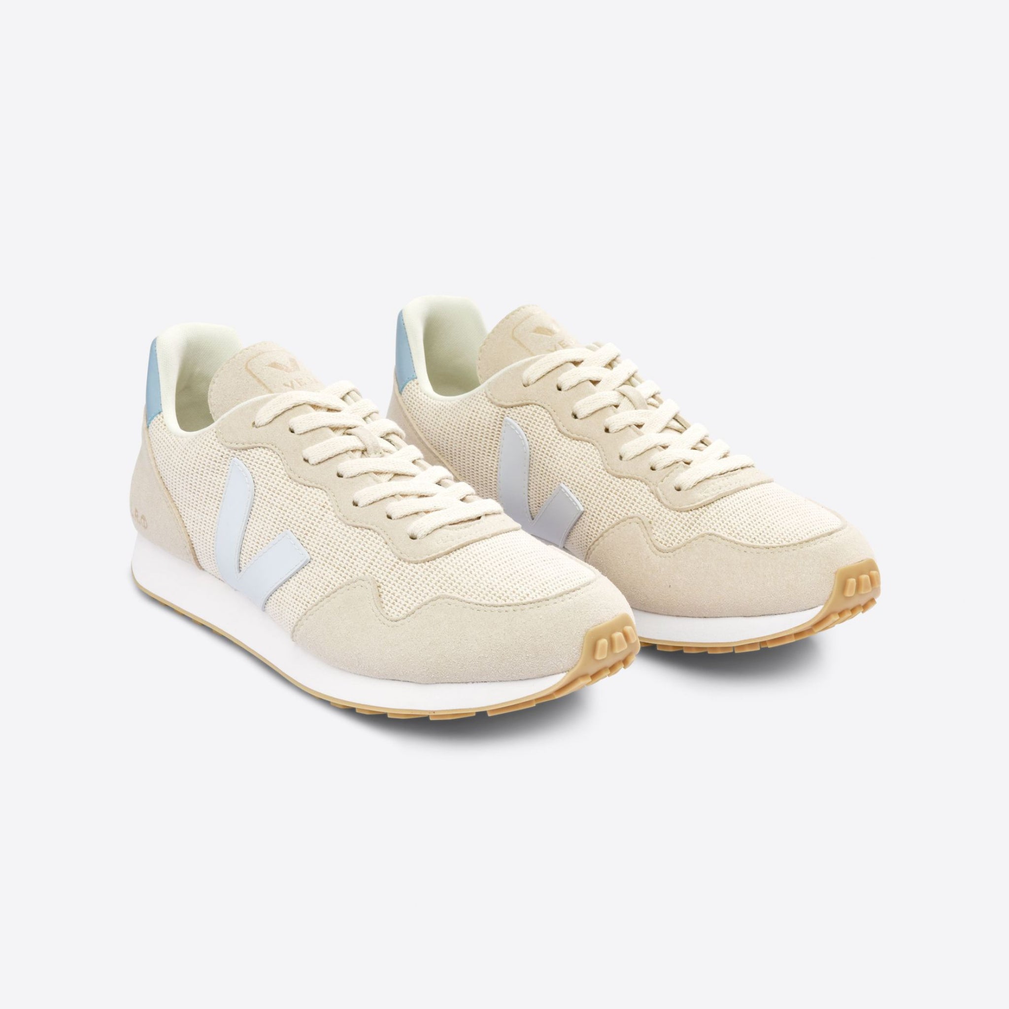 Beige Sneaker mit weißen Akzenten und blauen Fersenlaschen auf grauem Hintergrund.
