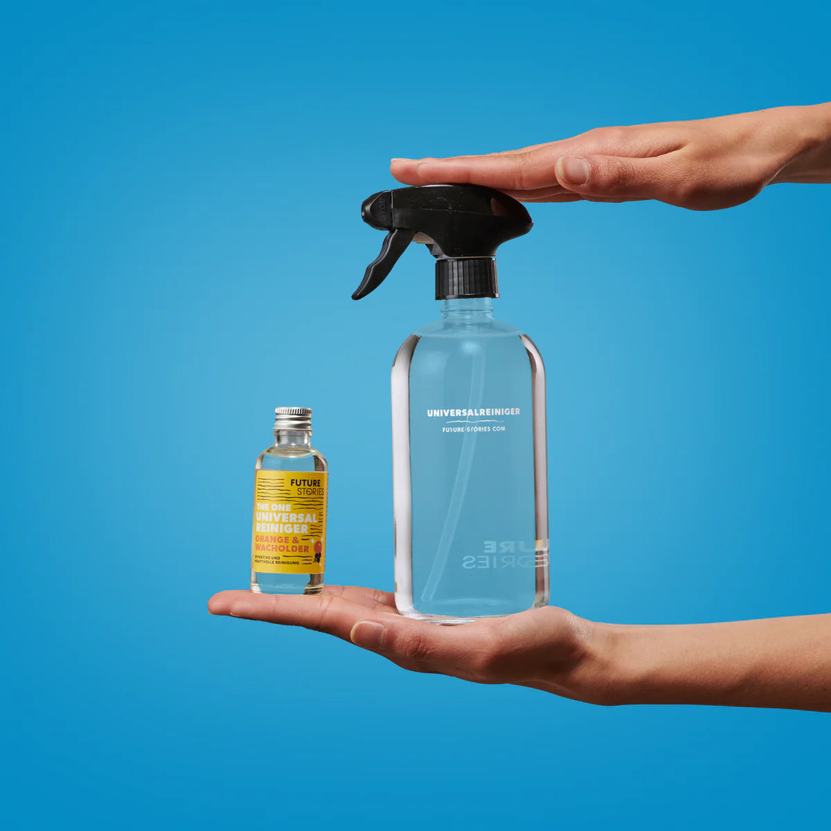Zwei Hände halten Reinigungsmittel: eine Hand hält eine kleine Flasche mit konzentriertem Reinigungsmittel, die andere eine größere, mit blauer Flüssigkeit gefüllte Sprühflasche, beide vor einem hellblauen Hintergrund.