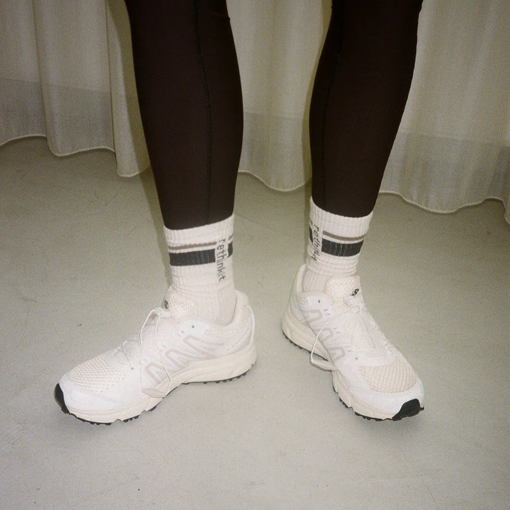 Beine in schwarzen Leggings mit weißen Socken und weißen Turnschuhen auf einem hellen Boden.