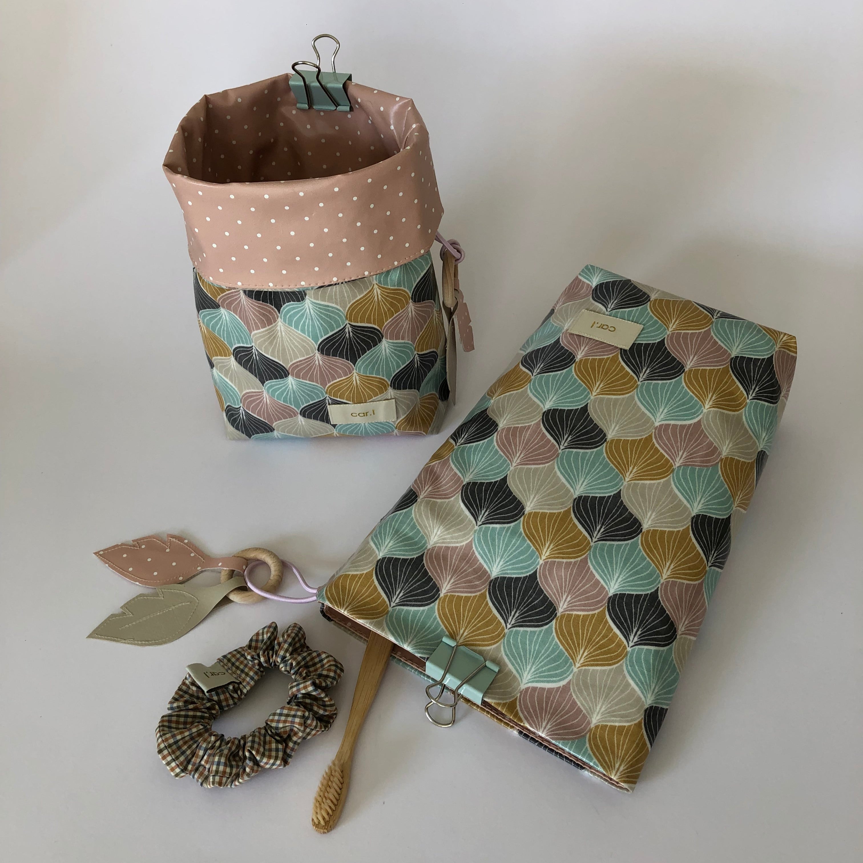 Korb und Stoffetui mit buntem Muster, daneben ein kariertes Haargummi, ein Holzring mit Blättern und eine Zahnbürste.