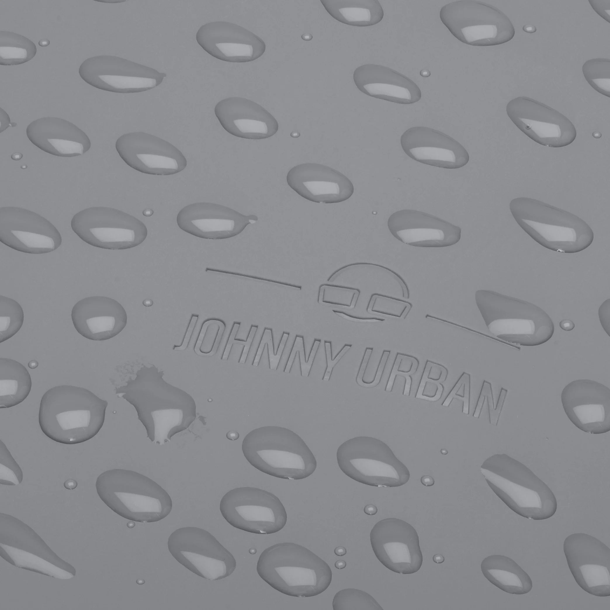 Nahaufnahme einer grauen Oberfläche mit Wassertropfen und dem eingeprägten Logo und Text JOHNNY URBAN in der Mitte.