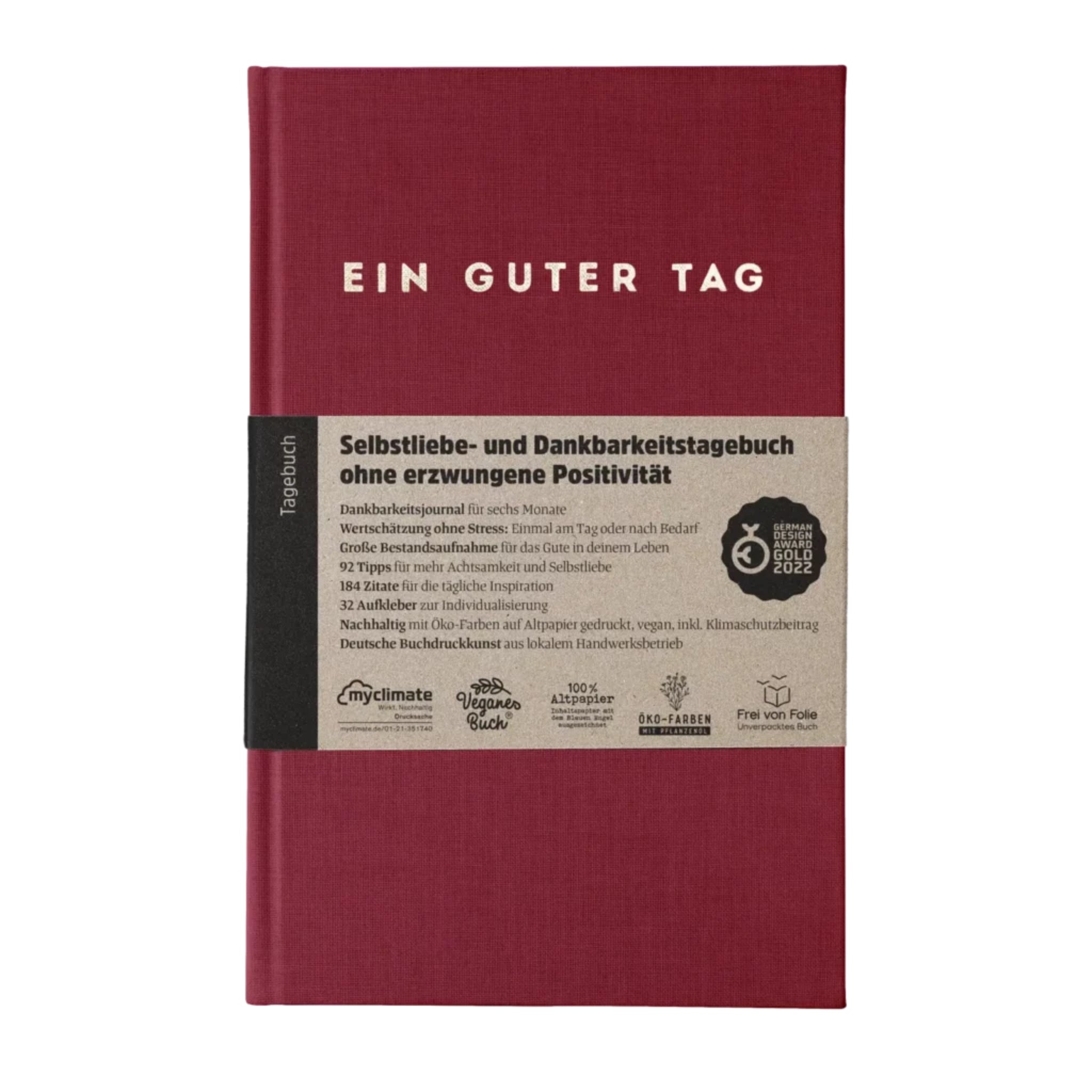 Rotes Tagebuch mit der Aufschrift "EIN GUTER TAG" und einem Papierband mit Informationen zum Dankbarkeitsjournal.