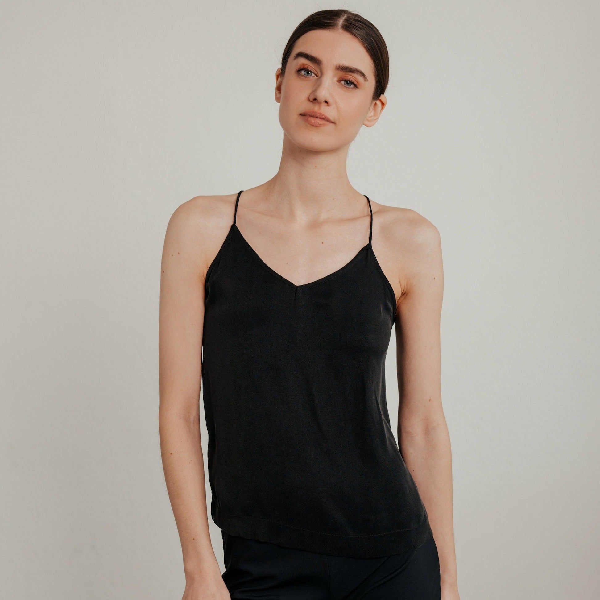 Frau in einem schwarzen Trägertop vor einem neutralen Hintergrund.