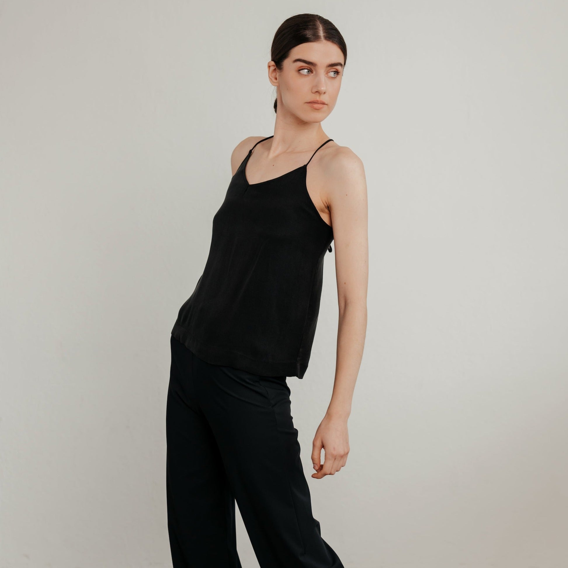 Junge Frau in schwarzer Kleidung posiert vor neutralem Hintergrund und schaut zur Seite.