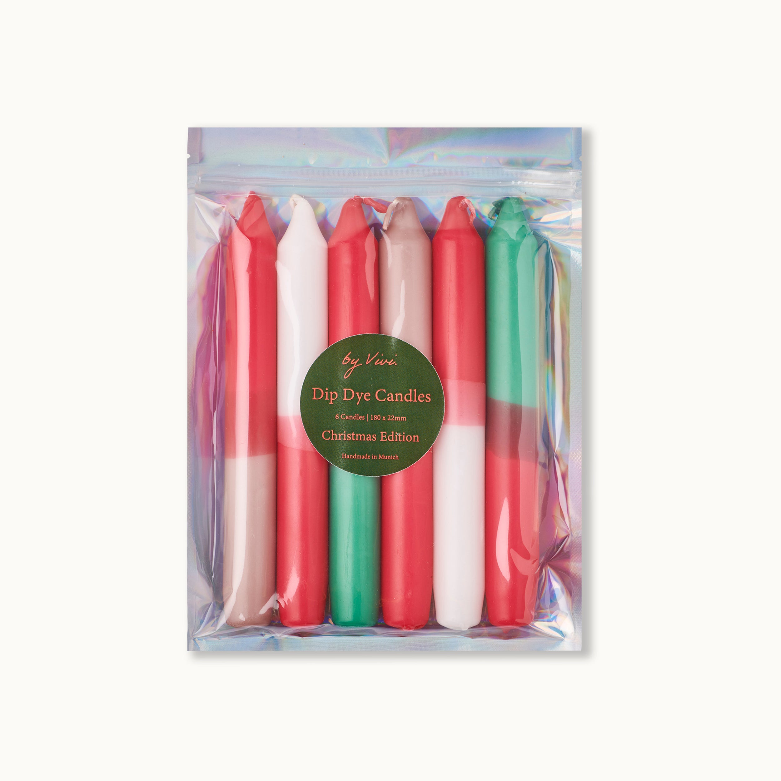Ein Set mit sechs bunten Dip-Dye-Kerzen in den Farben Rot, Weiß, Grün und Beige, verpackt in einer glänzenden, holografischen Tüte mit der Aufschrift Dip Dye Candles: Weihnachtsausgabe.