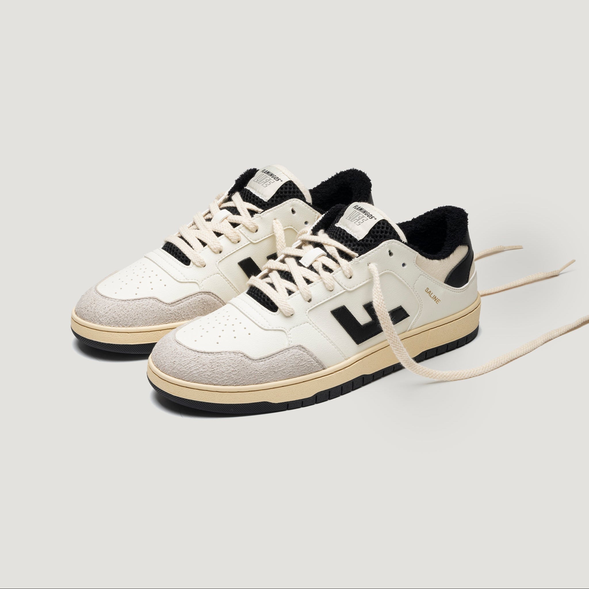 Ein Paar cremefarbene und beigefarbene Turnschuhe mit schwarzen Akzenten und Schnürsenkeln, mit einem schwarzen "V"-Logo an den Seiten, vor einem schlichten, hellen Hintergrund.