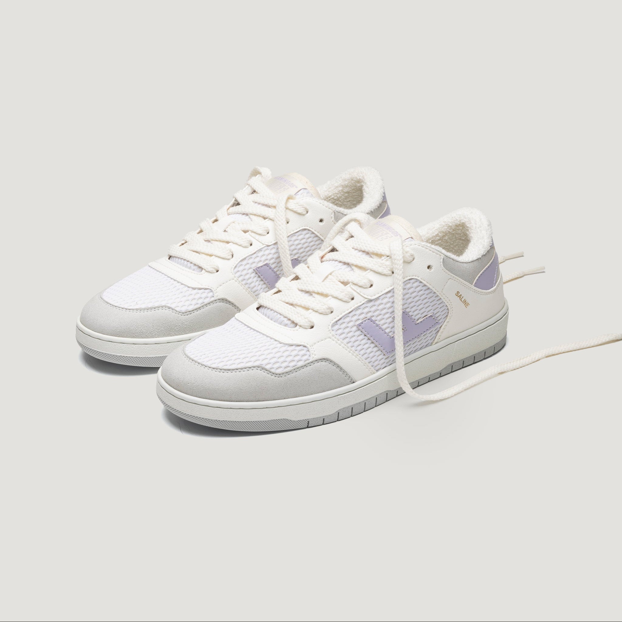 Ein Paar weiße und hellviolette Turnschuhe mit Mesh- und Wildlederdetails, weißen Schnürsenkeln und grauen Laufsohlen vor einem schlichten hellen Hintergrund.