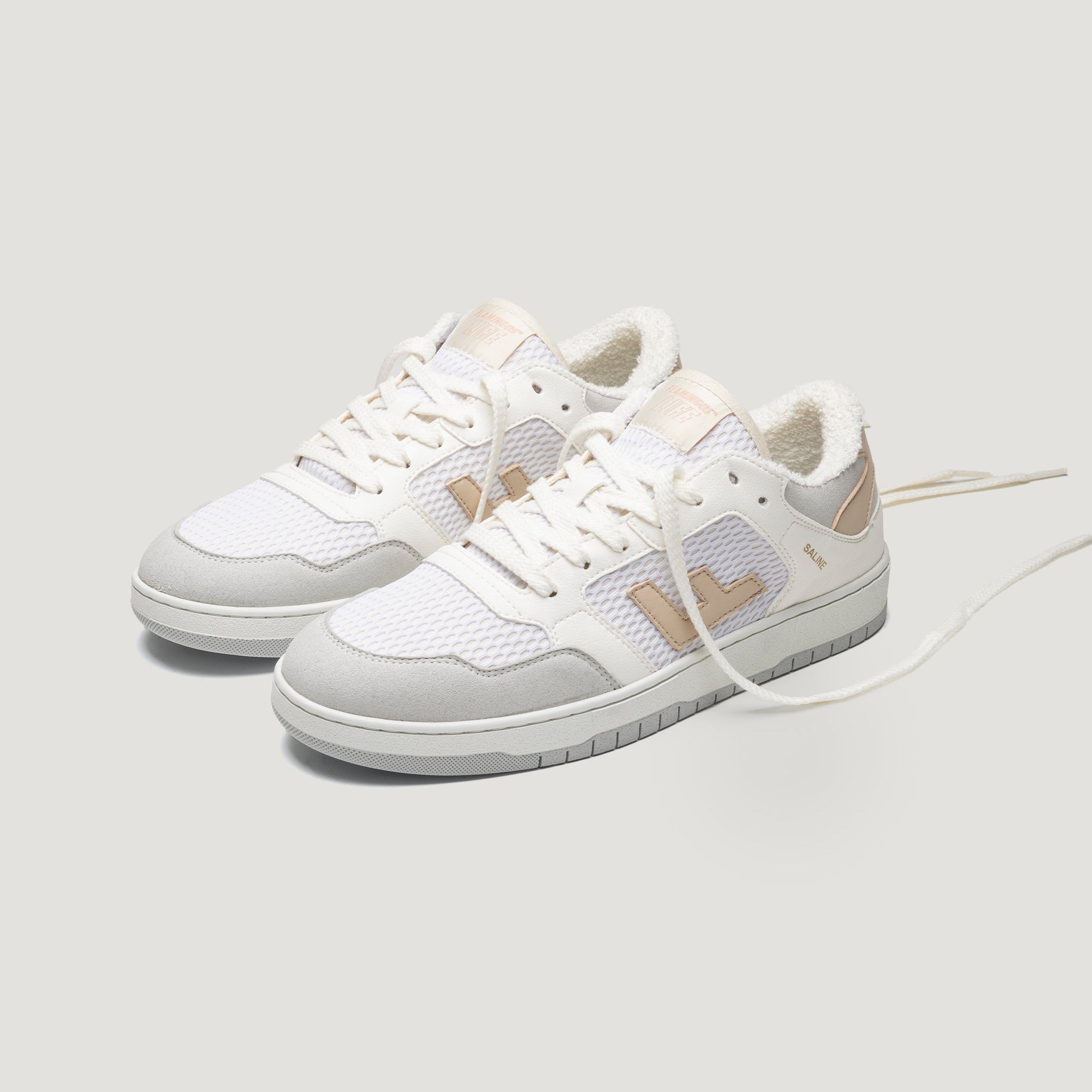 Ein Paar weiße und hellbeige Turnschuhe mit Details aus Mesh und Wildleder, weißen Schnürsenkeln und beigen Akzenten an den Seiten und der Ferse auf einem hellgrauen Hintergrund.