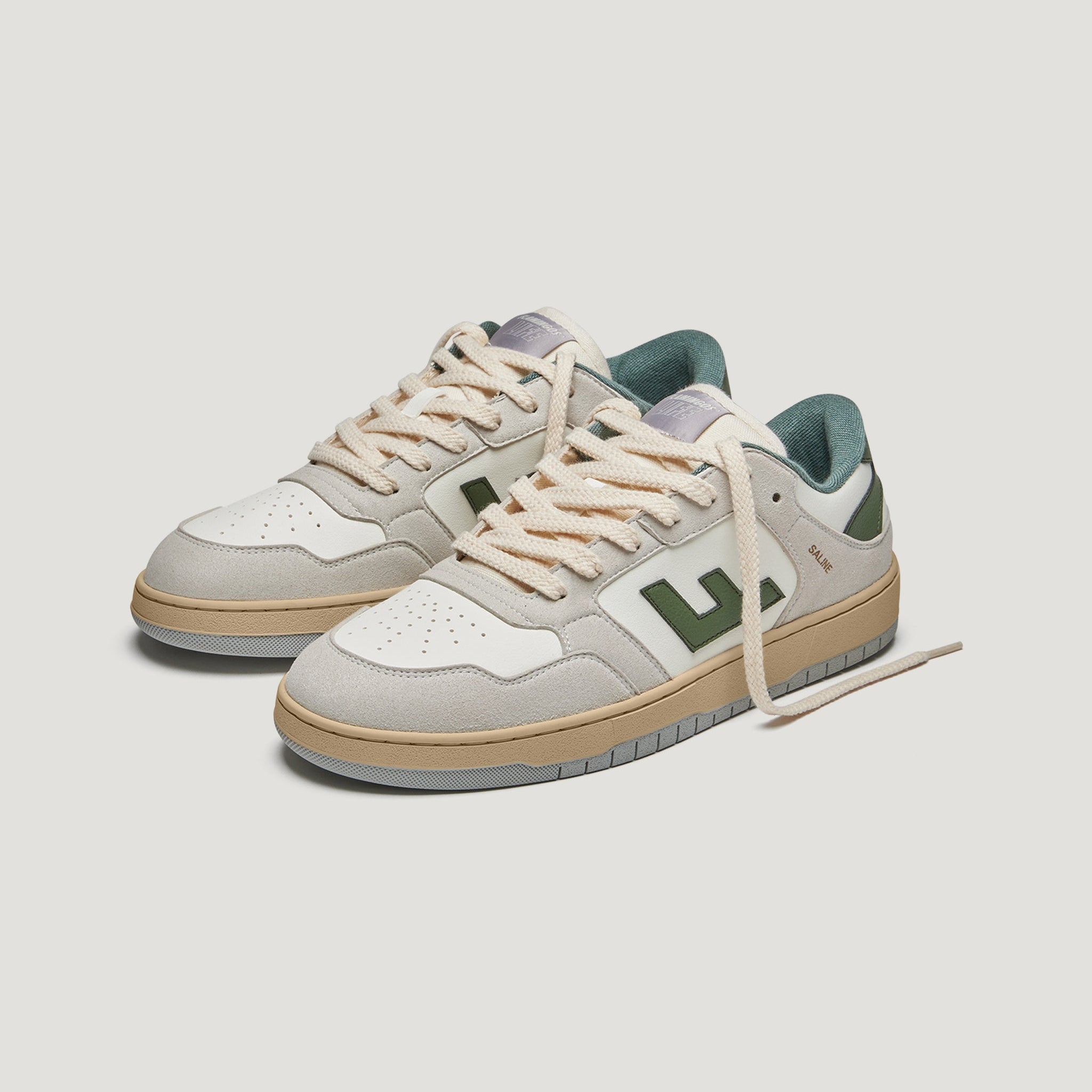 Ein Paar beige-weiße Turnschuhe mit grünen Akzenten, hellbraunen Sohlen und cremefarbenen Schnürsenkeln, die vor einem schlichten weißen Hintergrund stehen.