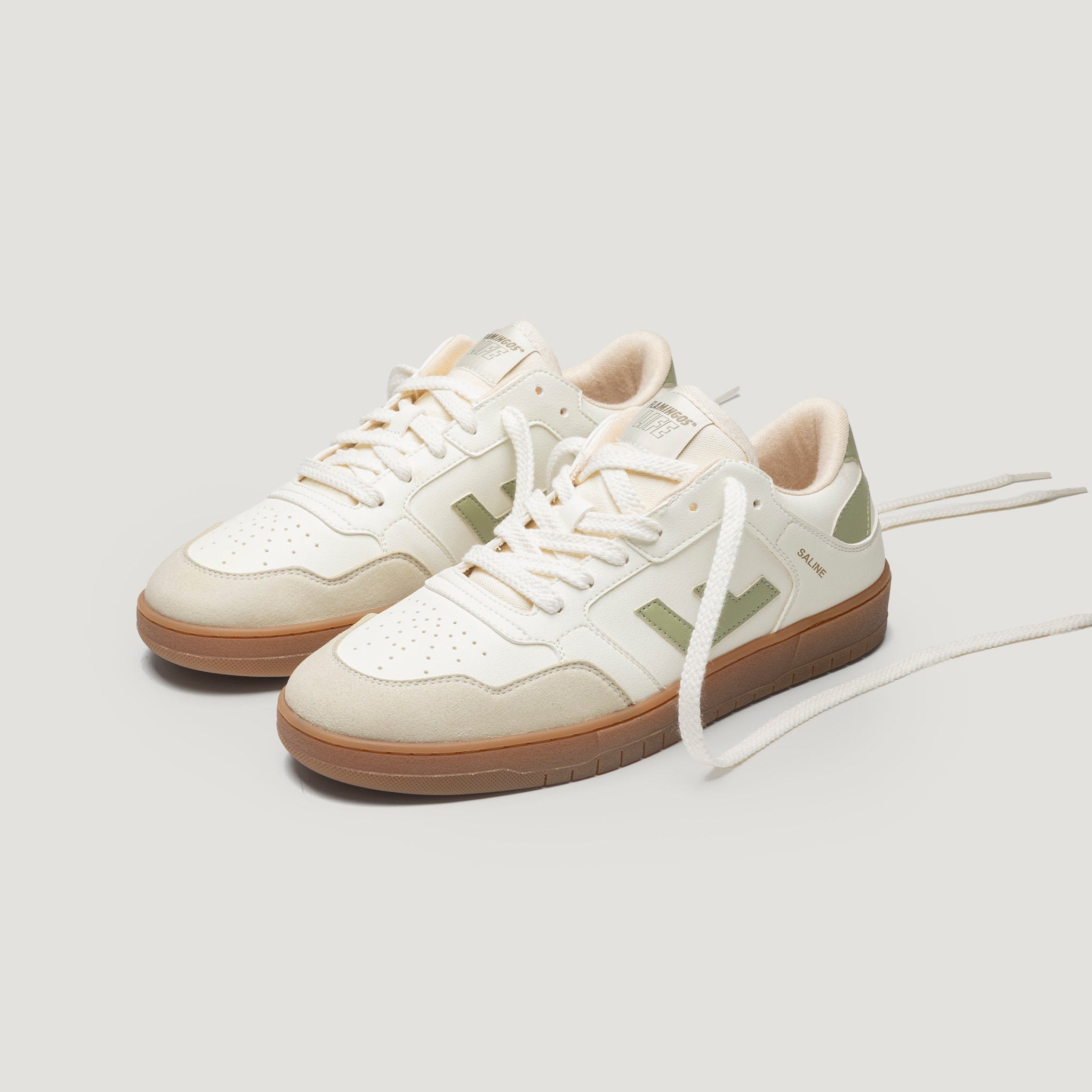 Ein Paar weiße und hellgrüne Turnschuhe mit beigen Akzenten, Gummisohlen und weißen Schnürsenkeln auf einem schlichten hellen Hintergrund. Die Schuhe stehen nebeneinander, wobei ein Schnürsenkel locker nach vorne gezogen ist.