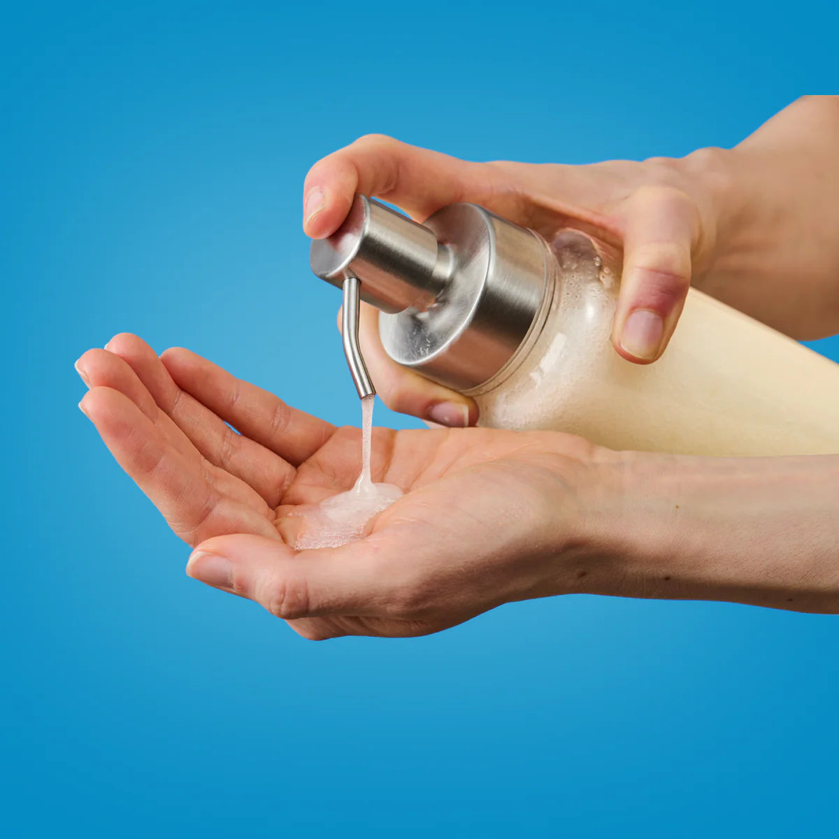 Zwei Hände, die Flüssigseife aus einer klaren Pumpflasche auf eine Handfläche verteilen, vor einem blauen Hintergrund.
