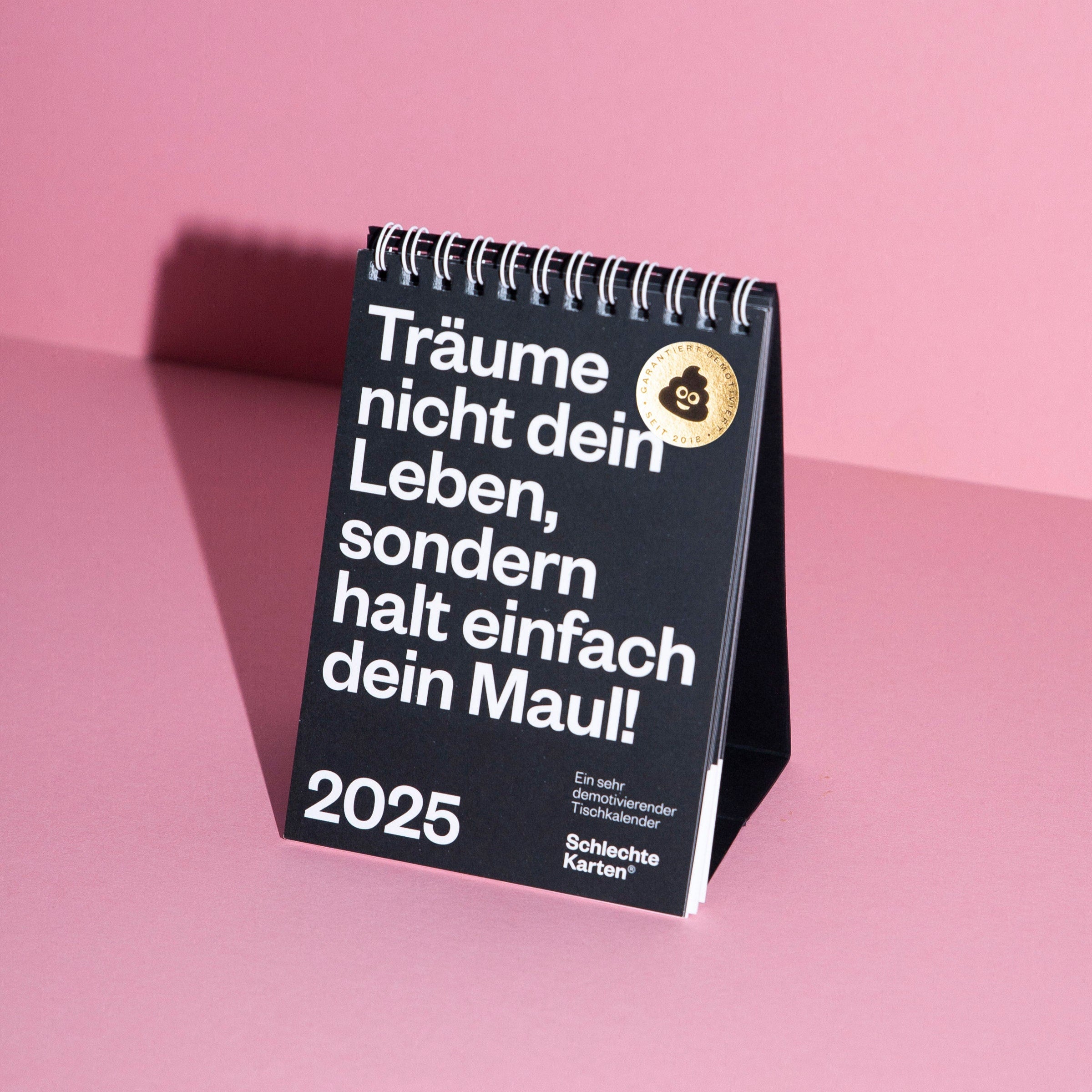 Schwarzer Tischkalender mit weißem Text auf rosa Hintergrund: "Träume nicht dein Leben, sondern halt einfach dein Maul!"