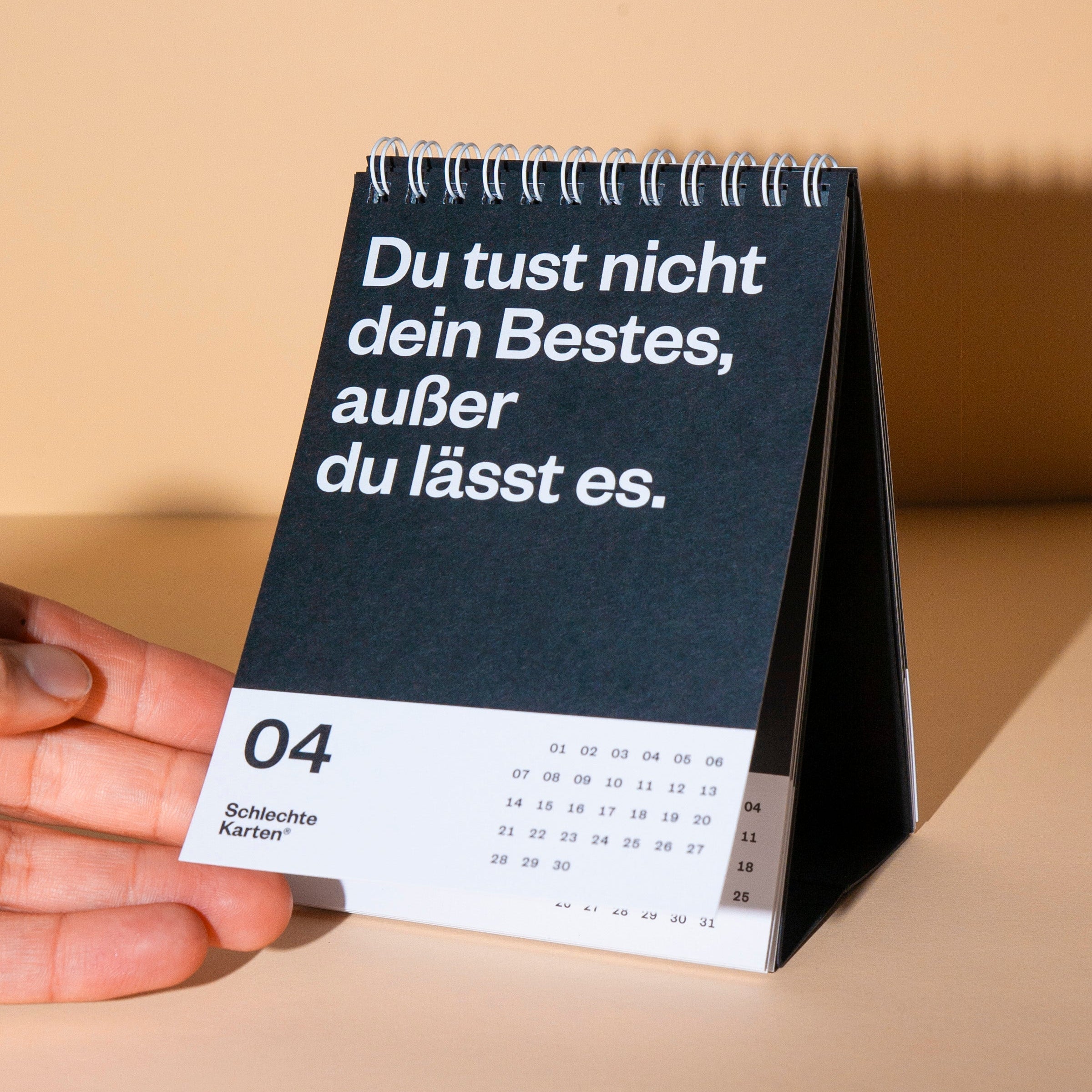 Tischkalender mit dem Zitat "Du tust nicht dein Bestes, außer du lässt es" auf schwarzem Hintergrund.