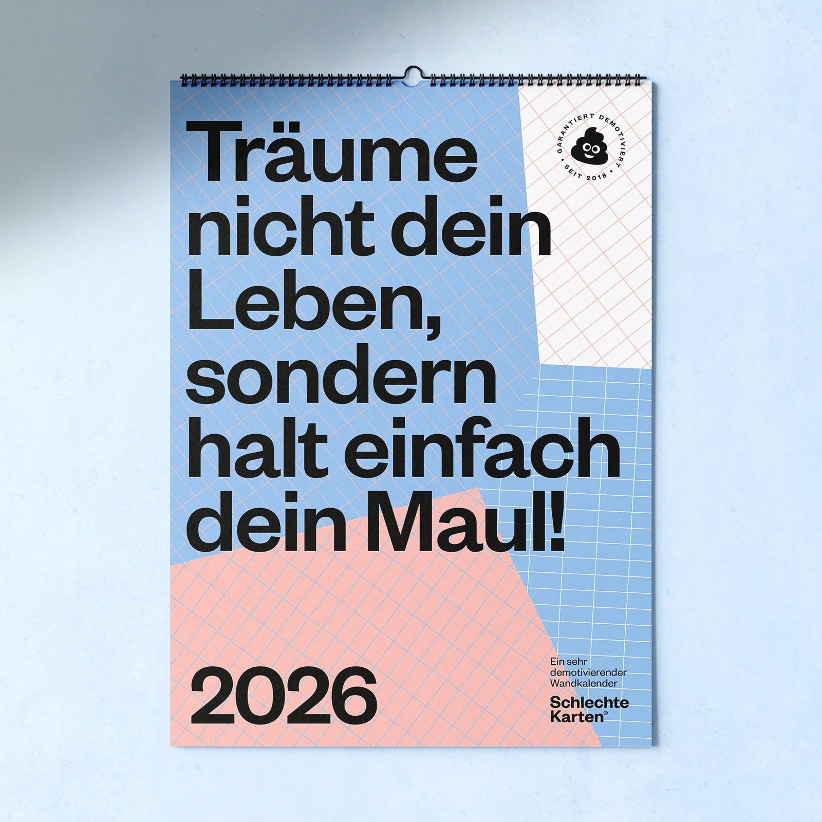 Ein Kalenderblatt mit einem geometrischen blau-rosa-weißen Gittermuster und einem großen deutschen Text: Träume nicht dein Leben, sondern halt einfach dein Maul! und die Jahreszahl 2026 am unteren Rand.