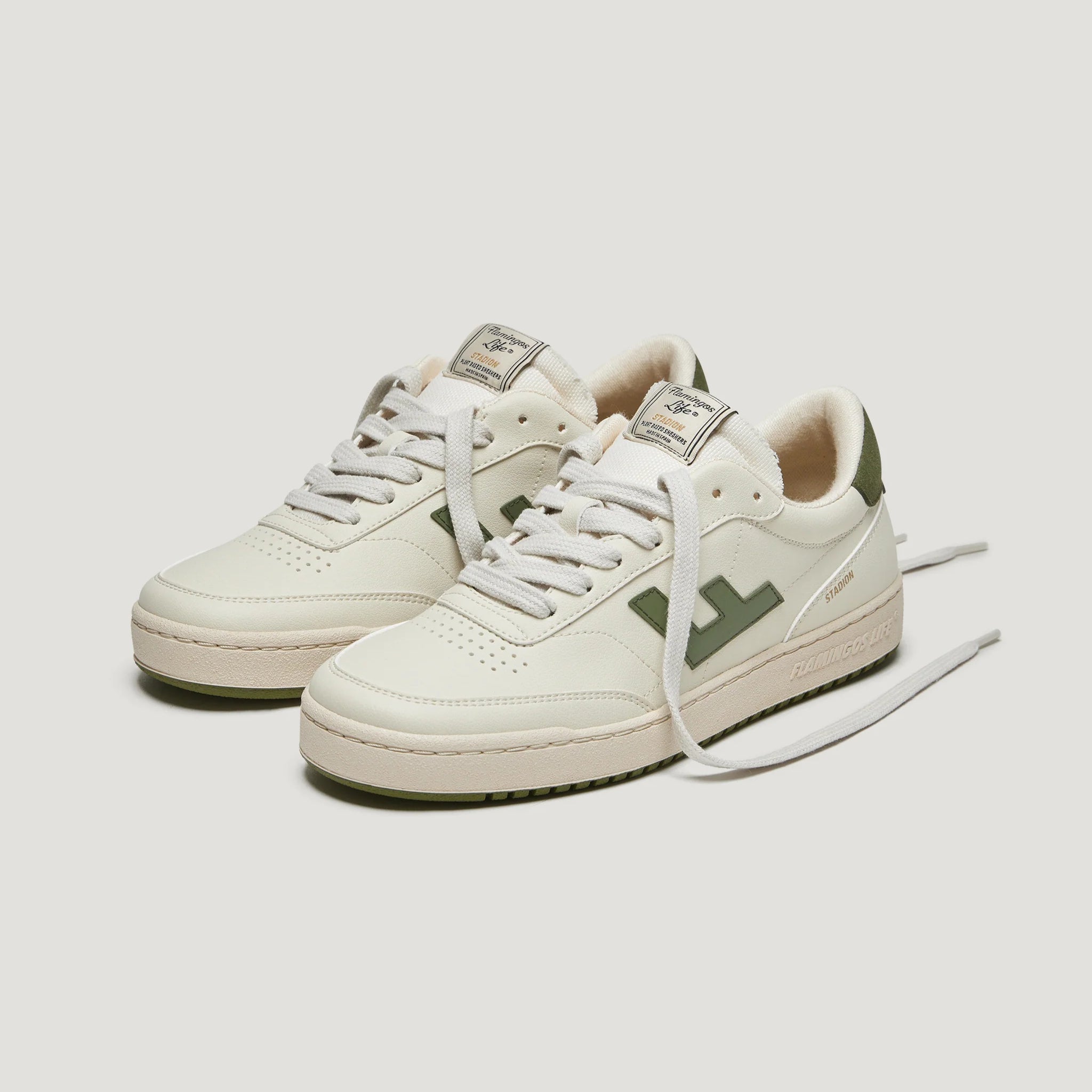 Weiße Turnschuhe mit grünen Details und Schnürsenkeln auf grauem Hintergrund.