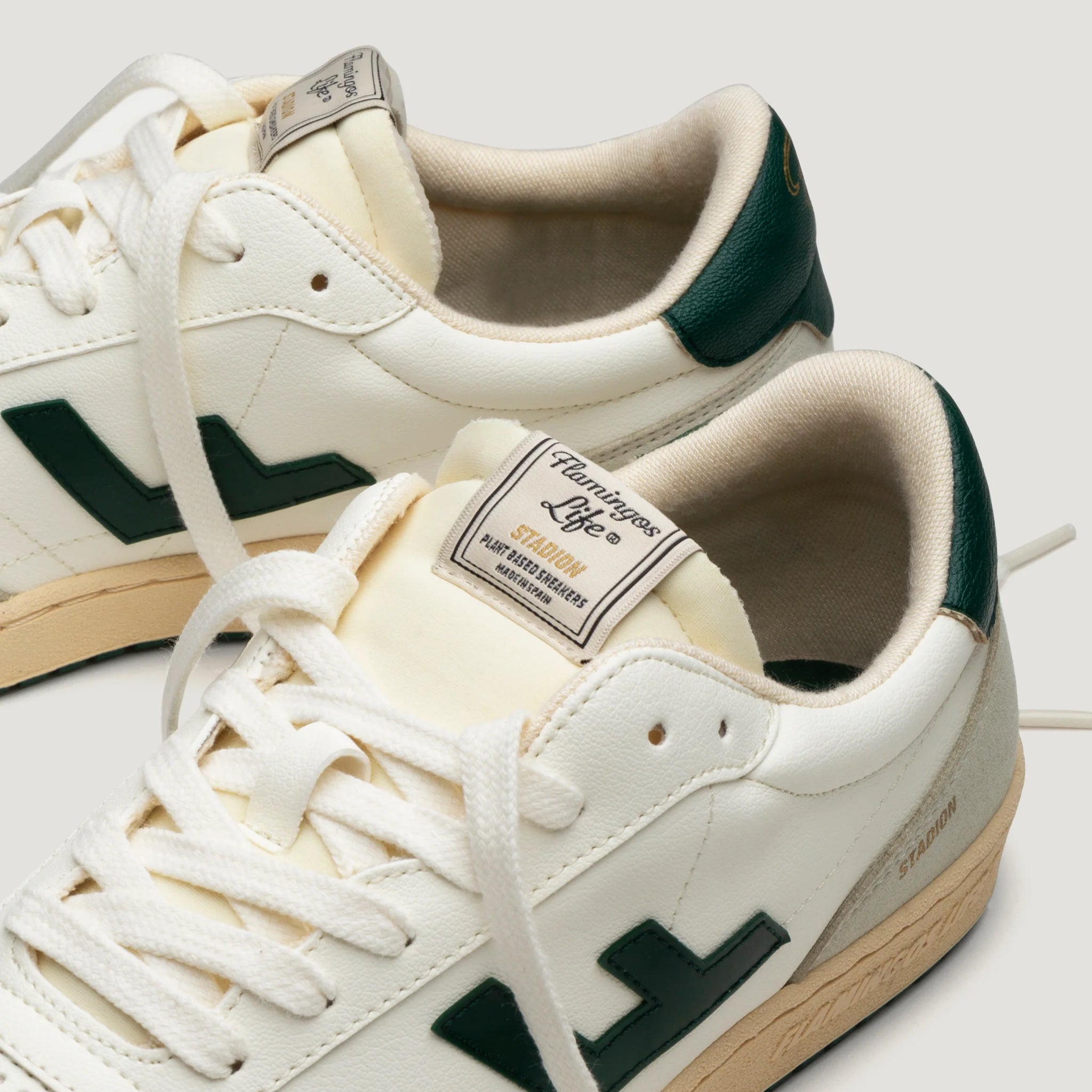 Weiße Sneaker mit grünen Details, Label "Flamingos Life" auf der Zunge, auf hellgrauem Hintergrund.