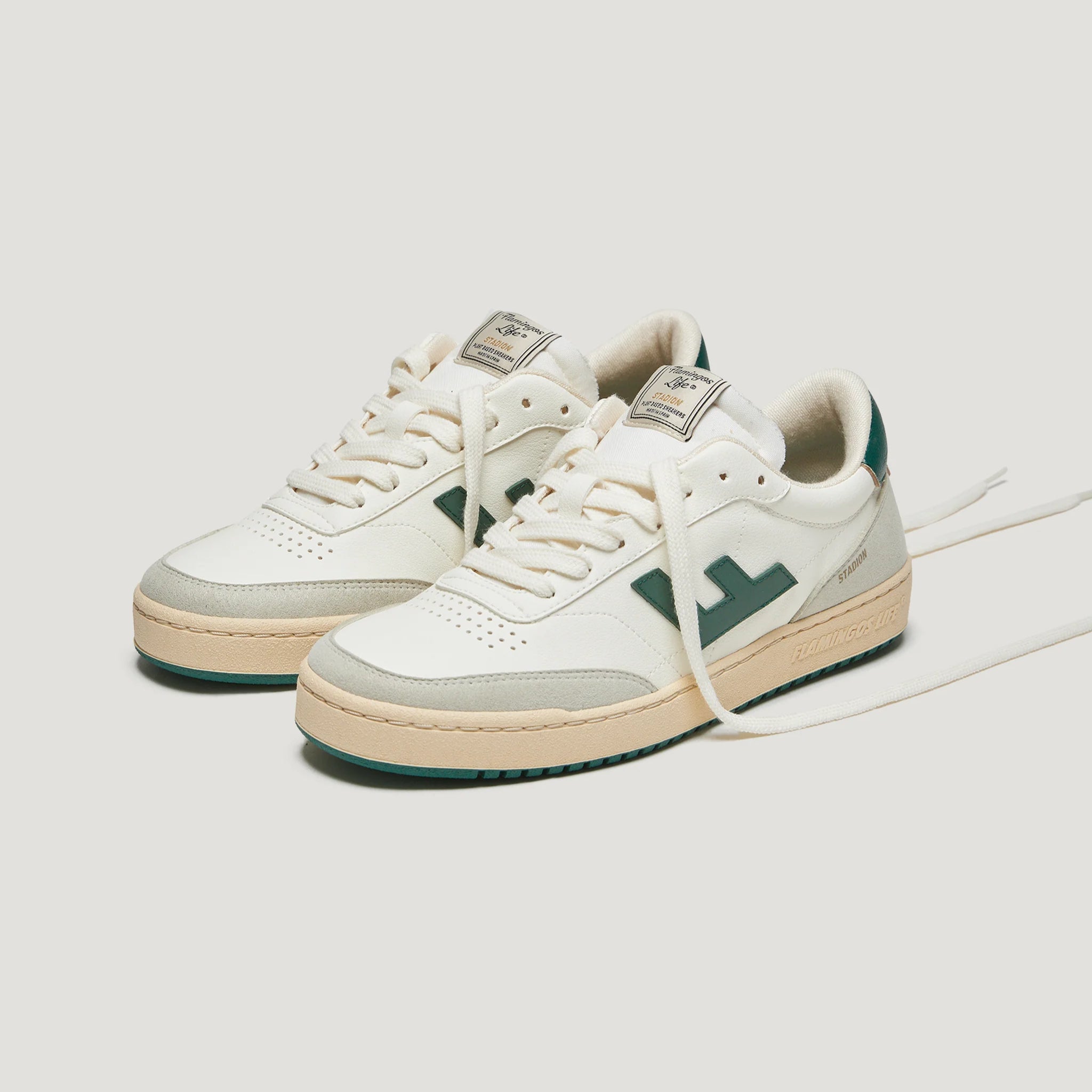 Weiße Sneaker mit grünen Details und beigem Akzent, seitlich fotografiert auf grauem Hintergrund.