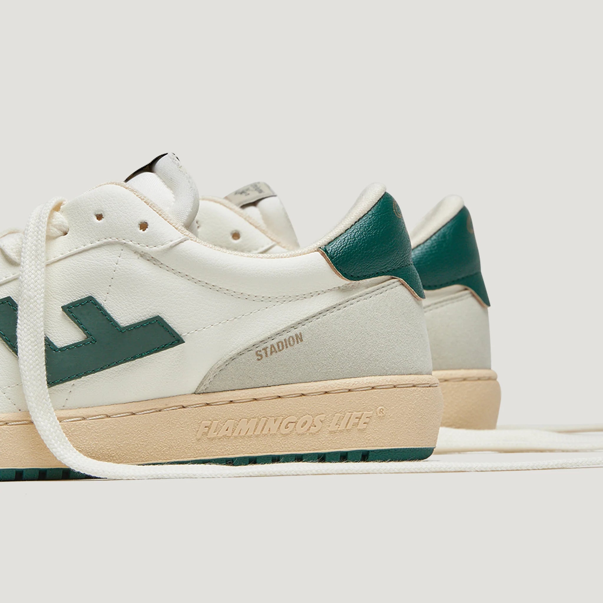 Weiße Sneakers mit grünen Details, seitlich ist "STADION" und auf der Sohle "FLAMINGO'S LIFE" eingeprägt.