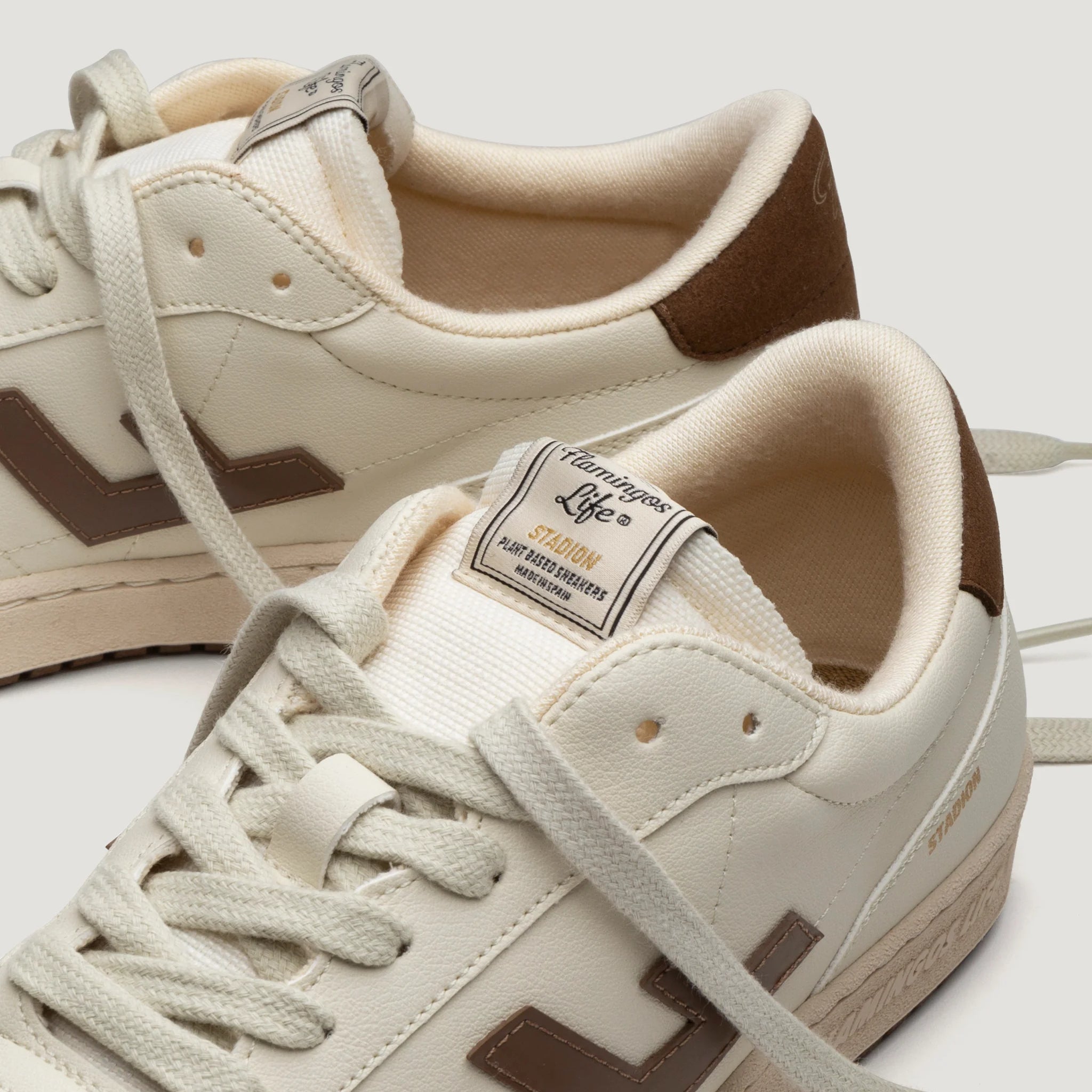 Beige Sneaker mit braunen Details und heller Sohle auf weißem Hintergrund, mit Markenetikett auf der Zunge.
