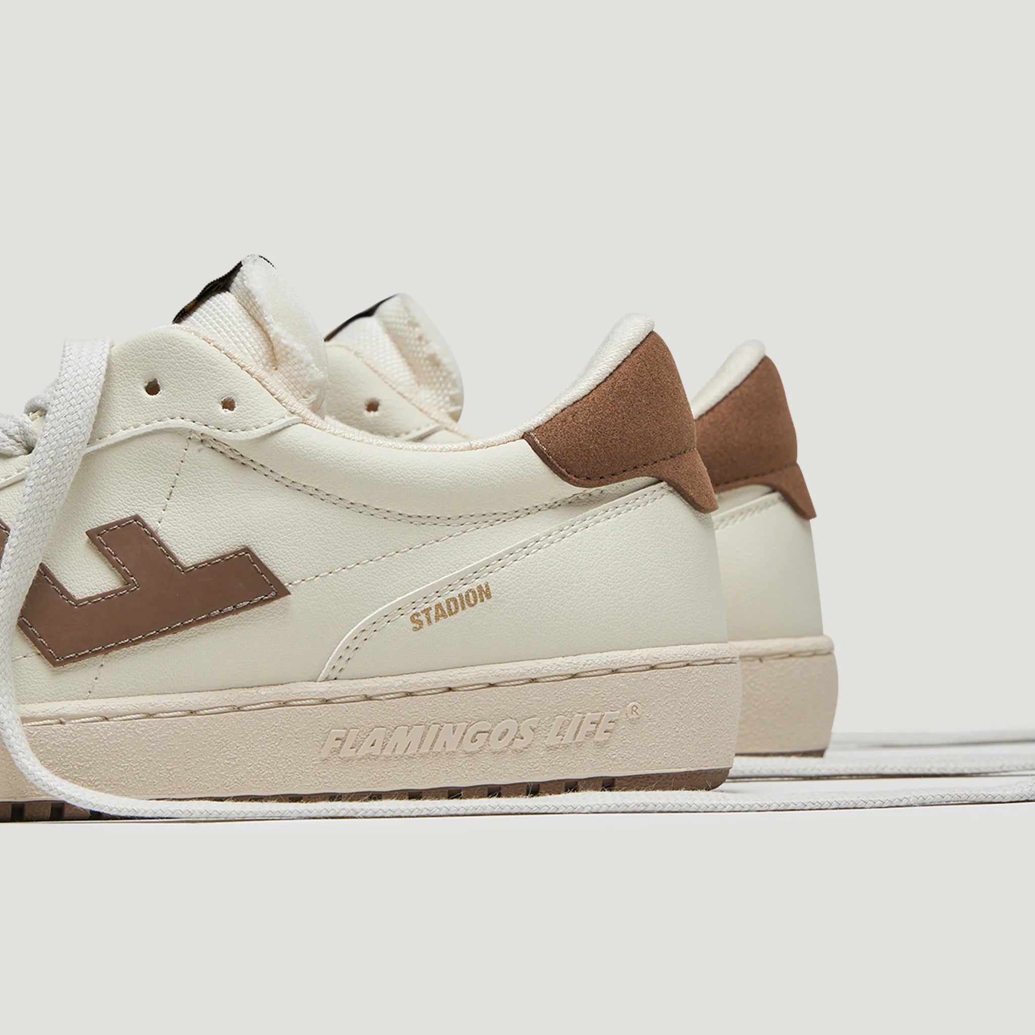 Weiße Sneaker mit braunen Akzenten und goldener Schrift "STADION" sowie geprägtem Logo "FLAMINGOS LIFE" auf der Sohle.