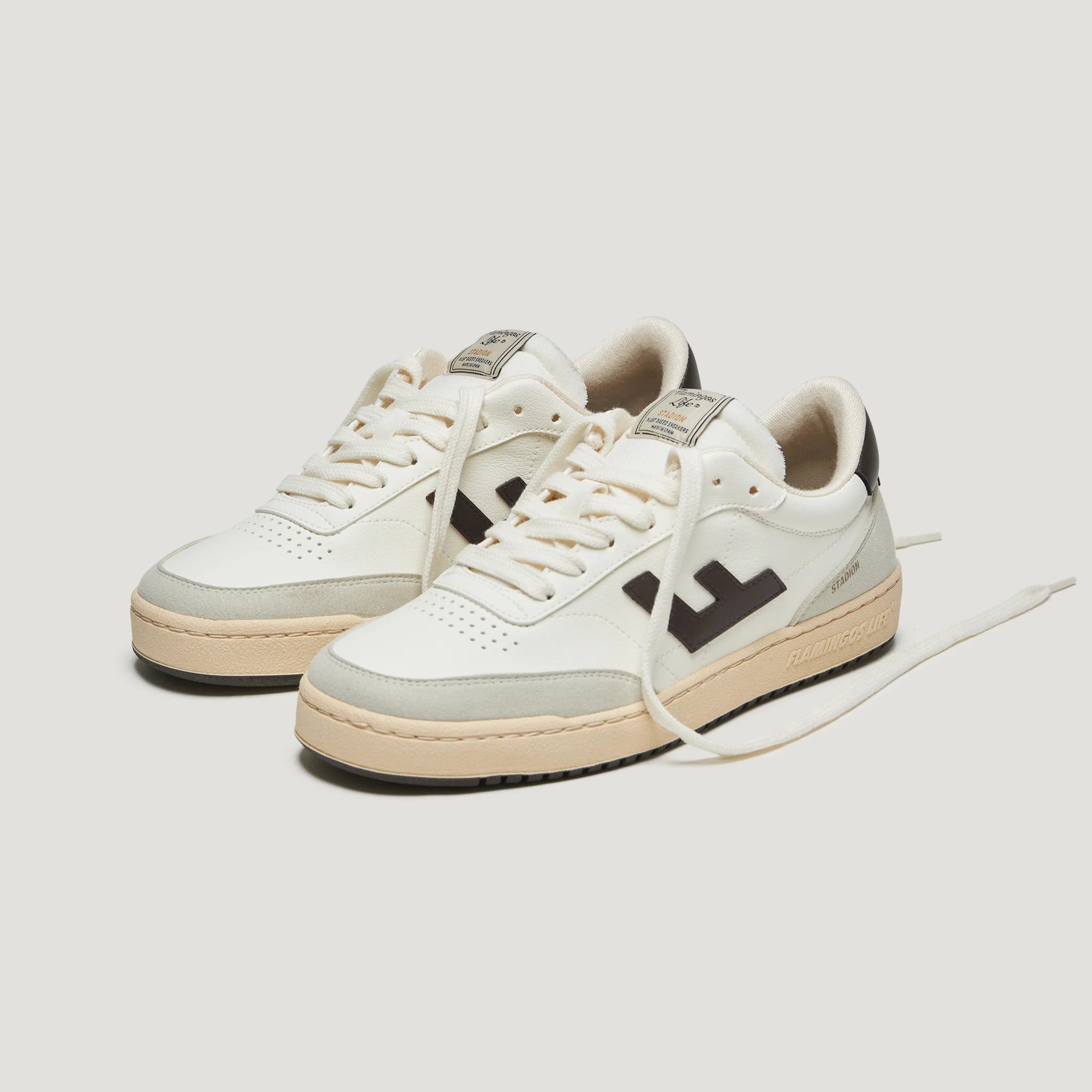 Weiße Sneakers mit braunen Details und dicker Sohle, auf hellgrauem Hintergrund.