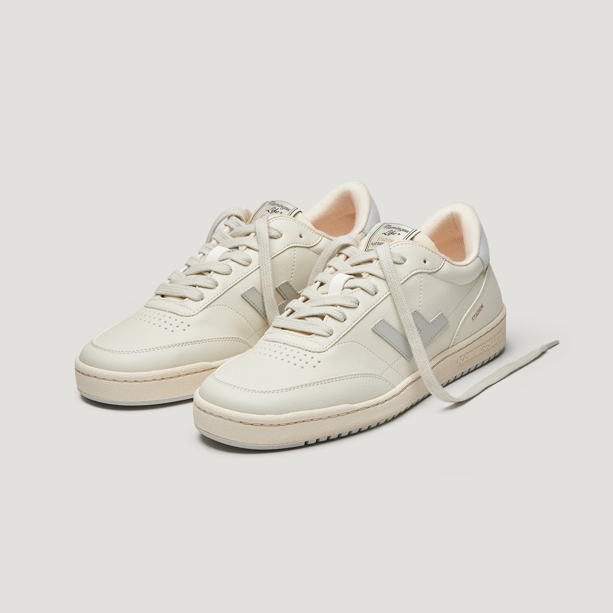 Zwei cremefarbene Sneaker mit grauen Details und weißen Schnürsenkeln auf weißem Hintergrund.
