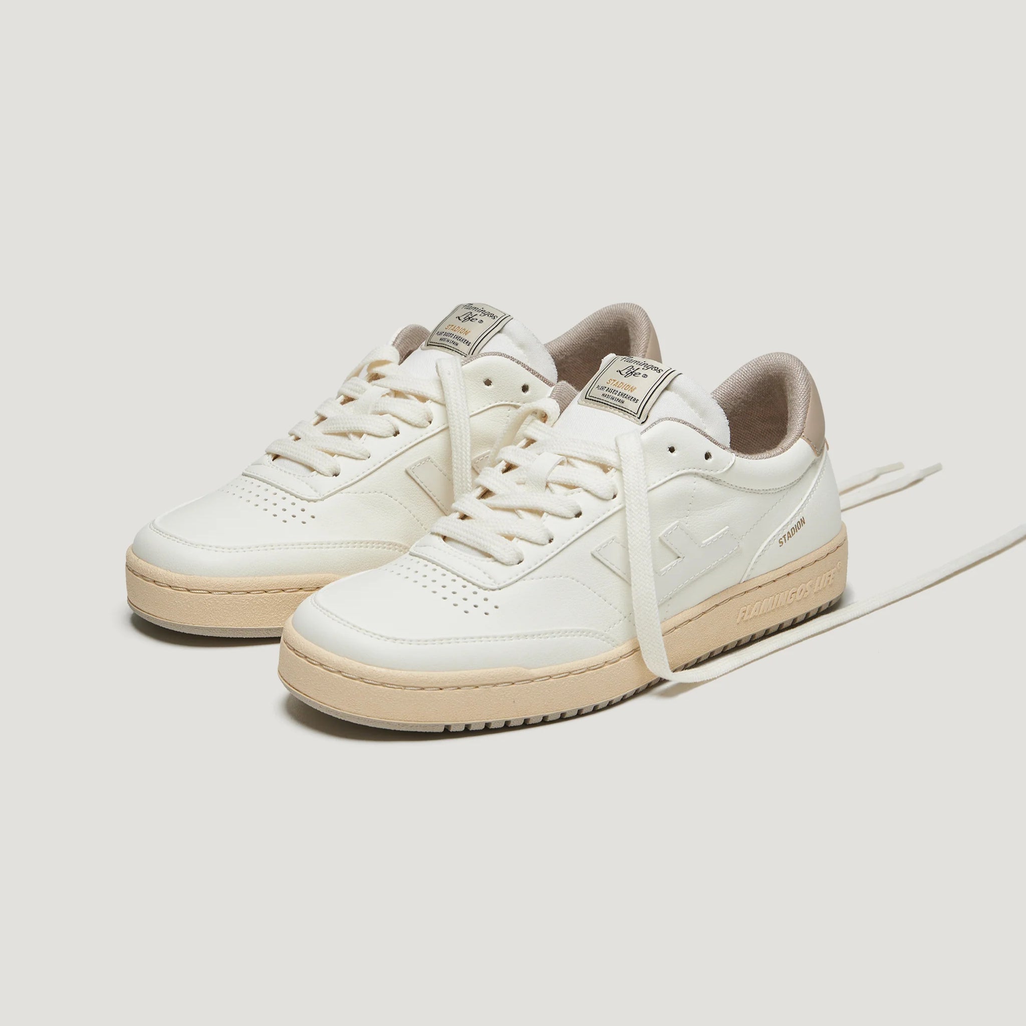 Weiße Sneakers mit beigefarbener Sohle auf neutralem Hintergrund, eine Lasche zeigt eine Herstellermarke.
