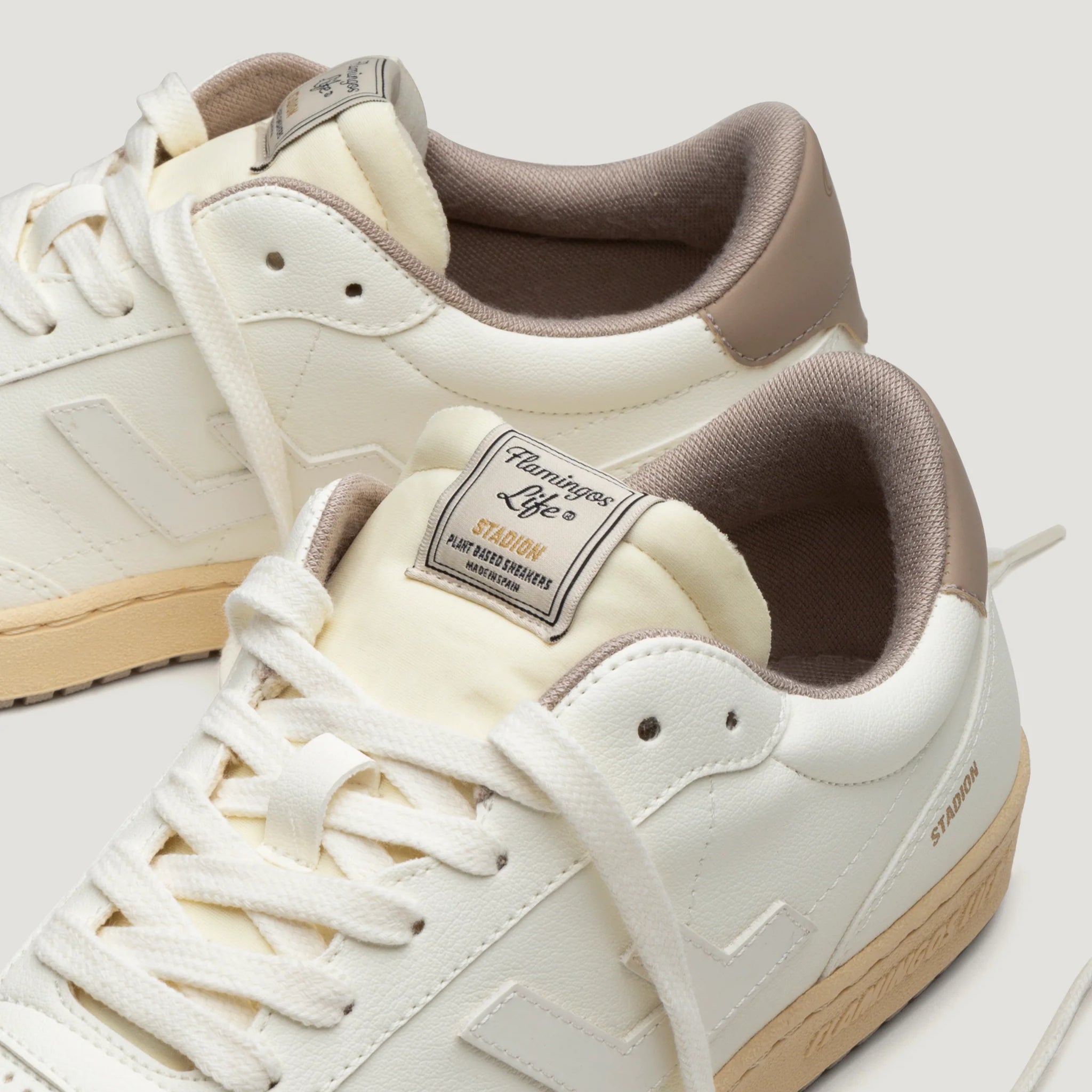 Weiße Sneaker mit beigem Rand und brauner Sohle, mit der Aufschrift "Flamingos Life" auf der Zunge.