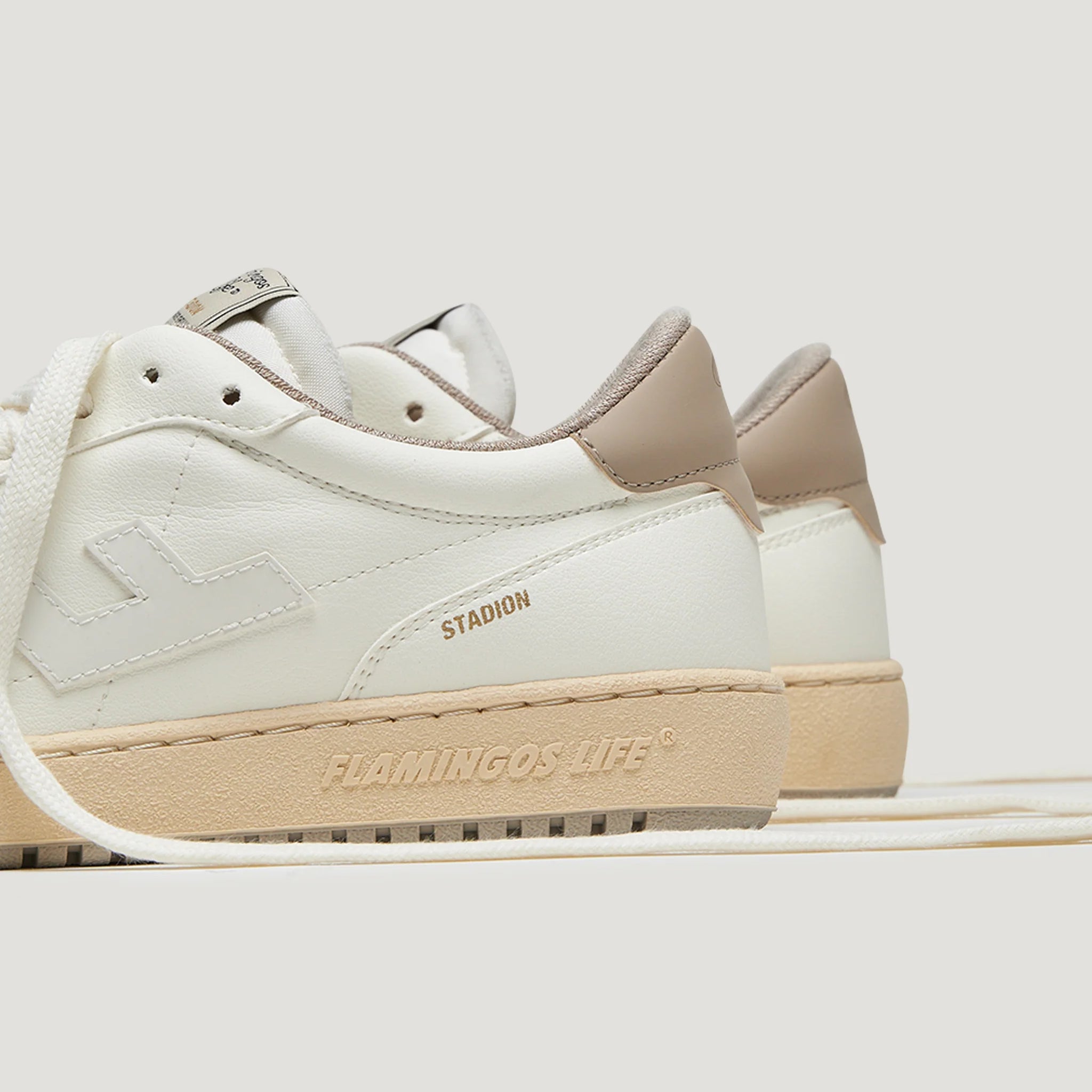 Weiße Sneaker mit beigem Akzent, seitlich mit „FLAMINGOS LIFE“ und „STADION“ graviert, auf hellem Hintergrund.