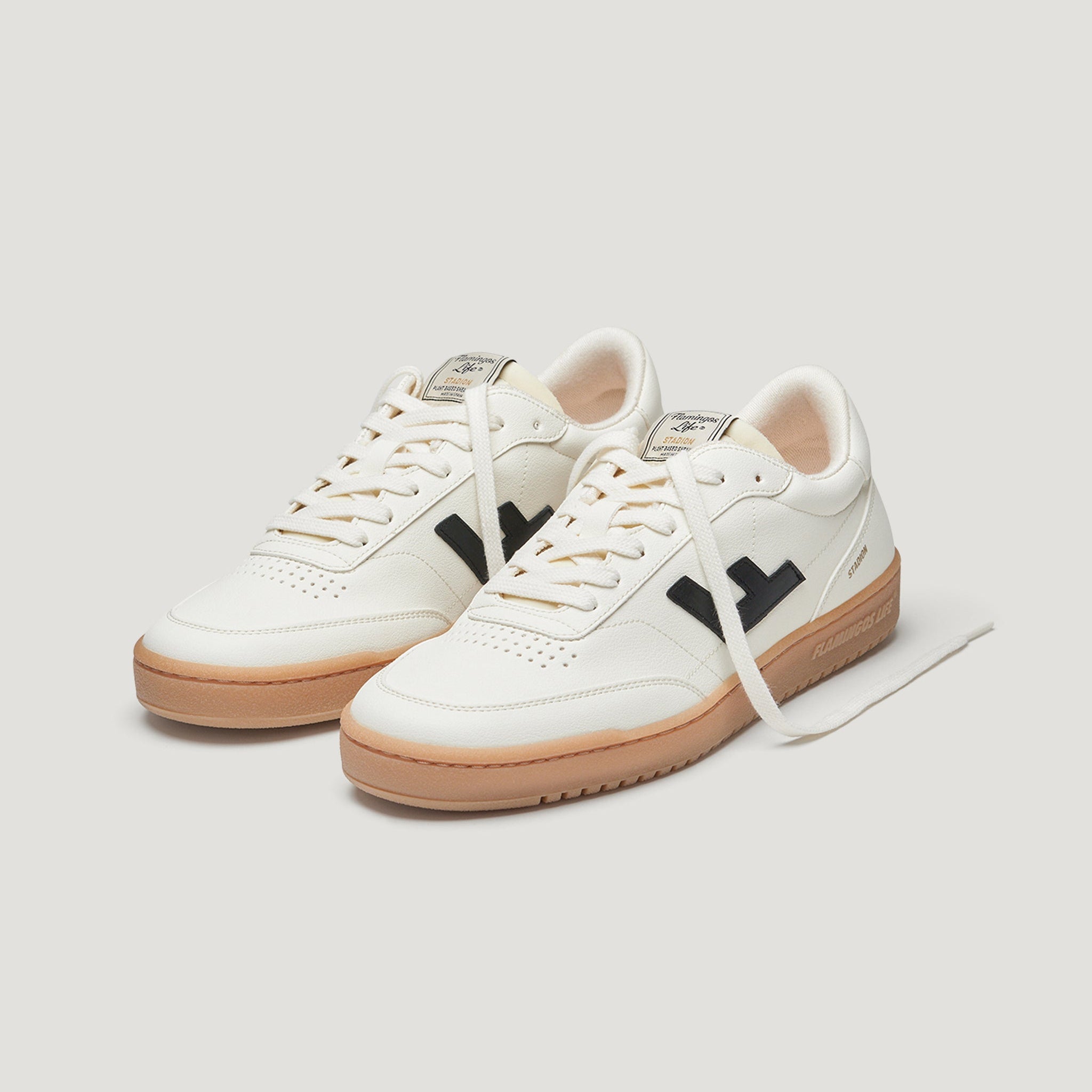 Ein Paar weiße Low-Top-Sneakers mit beigen Sohlen, schwarzen seitlichen Logo-Akzenten und weißen Schnürsenkeln auf einem schlichten hellen Hintergrund.