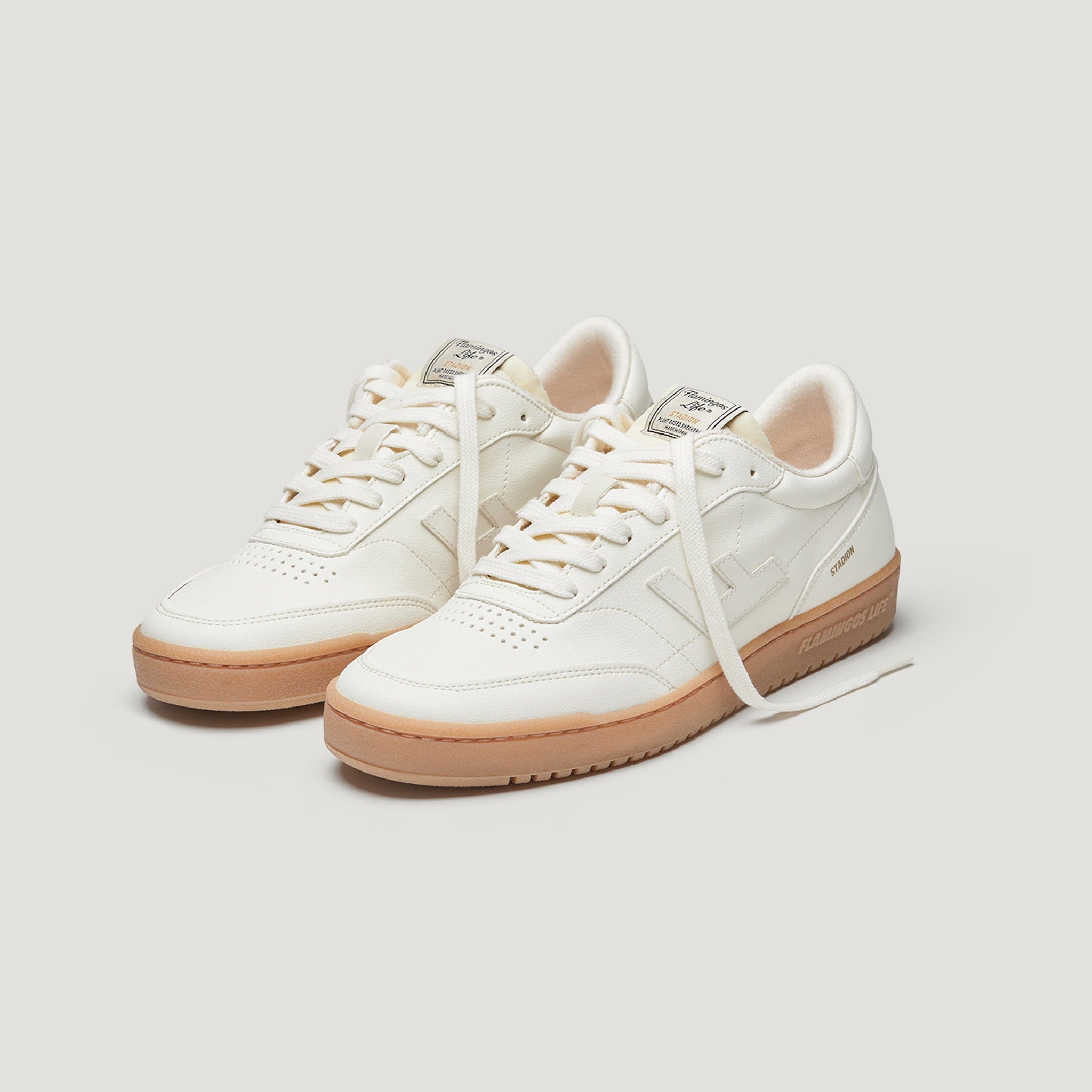 Ein Paar weiße Low-Top-Sneaker mit beigen Gummisohlen, weißen Schnürsenkeln und dezentem Branding an den Seiten und auf der Zunge vor einem schlichten, hellen Hintergrund.