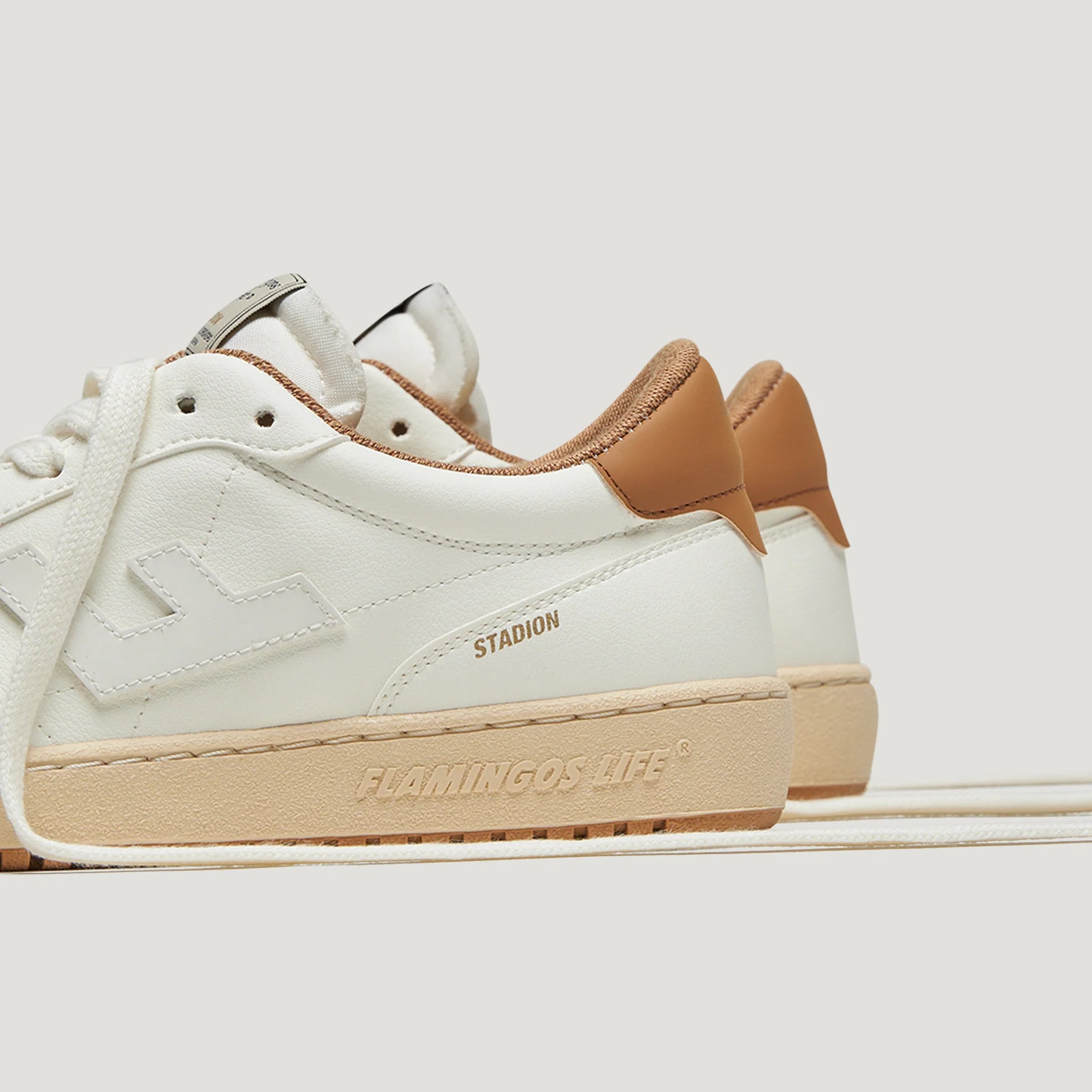 Weiße Sneaker mit braunen Akzenten und der Aufschrift "Flamingos Life" und "Stadion" auf der Seite.