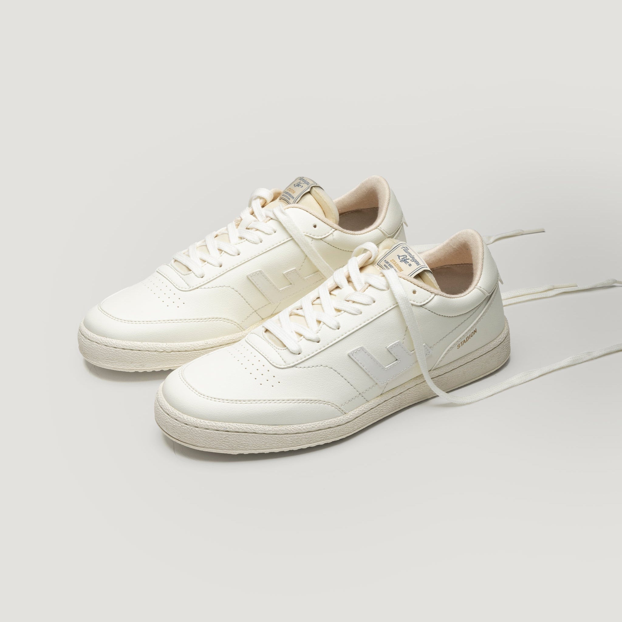 Ein Paar cremefarbene Ledersneaker mit hellbeigen Akzenten, passenden Schnürsenkeln und minimalistischem Design, fotografiert vor einem schlichten hellgrauen Hintergrund.