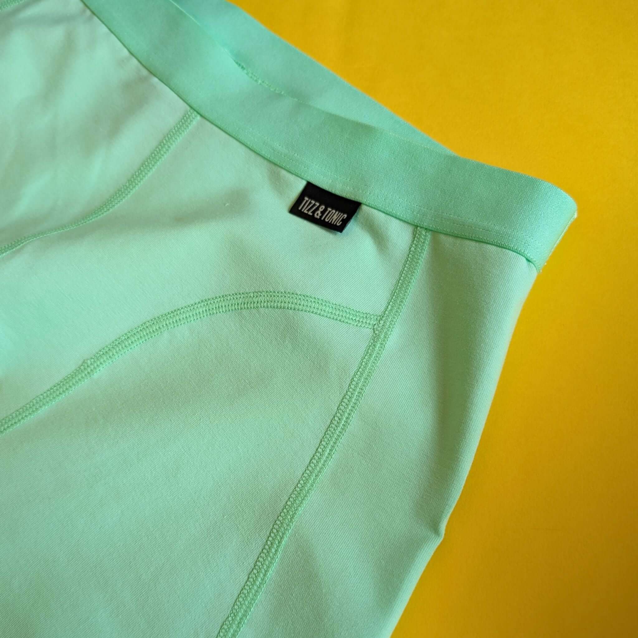 Mintgrüne Shorts auf gelbem Hintergrund, mit sichtbarem Etikett.