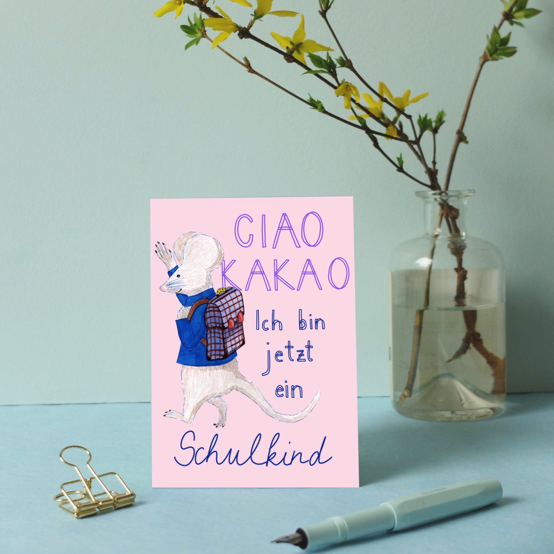 Karte mit einer gezeichneten Maus und der Aufschrift "CIAO KAKAO, Ich bin jetzt ein Schulkind", daneben Vase mit Zweig.