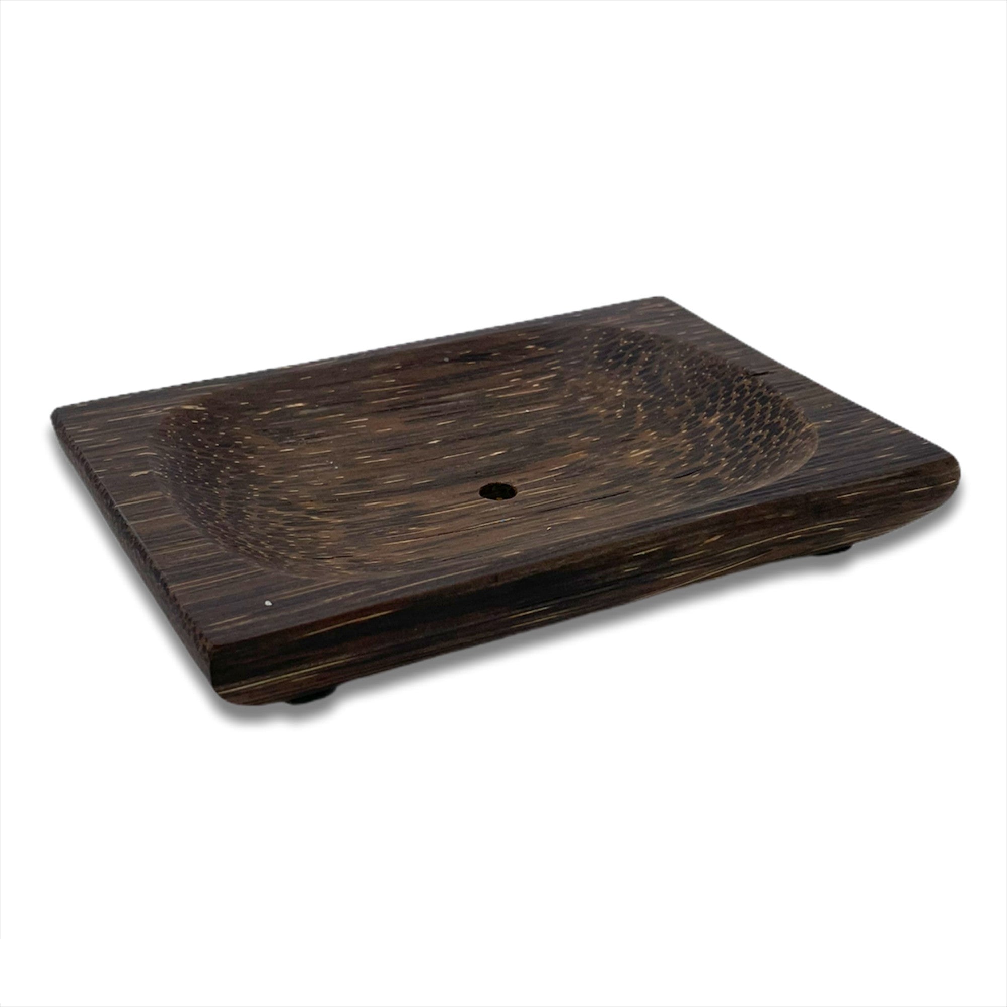 Eine rechteckige Seifenschale aus dunklem Holz mit einer leicht gewölbten Mitte, einem kleinen Abflussloch und vier kleinen Füßen, von einem Winkel aus gesehen auf einem weißen Hintergrund.