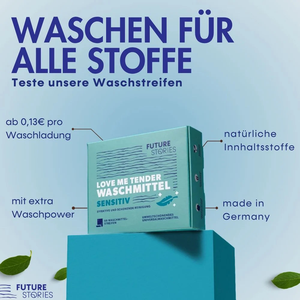 Eine blaue Schachtel mit "Love Me Tender Waschmittel"-Streifen wird auf einer blauen Plattform präsentiert. Der Text hebt die Eigenschaften hervor: für alle Textilien geeignet, umweltfreundlich, natürliche Inhaltsstoffe, zusätzliche Waschkraft und hergestellt in Deutschland.