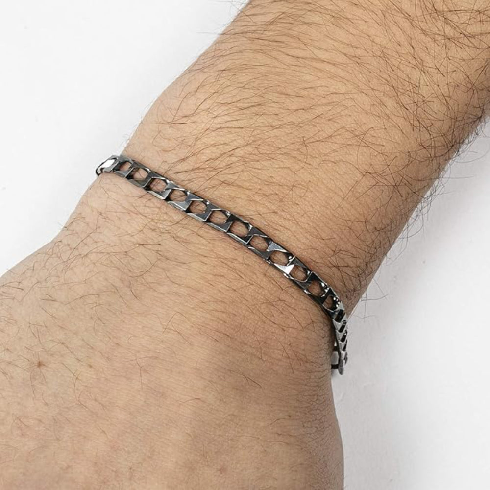 Nahaufnahme eines Handgelenks mit einem dünnen, silberfarbenen Kettenarmband mit rechteckigen Gliedern vor einem schlichten weißen Hintergrund.