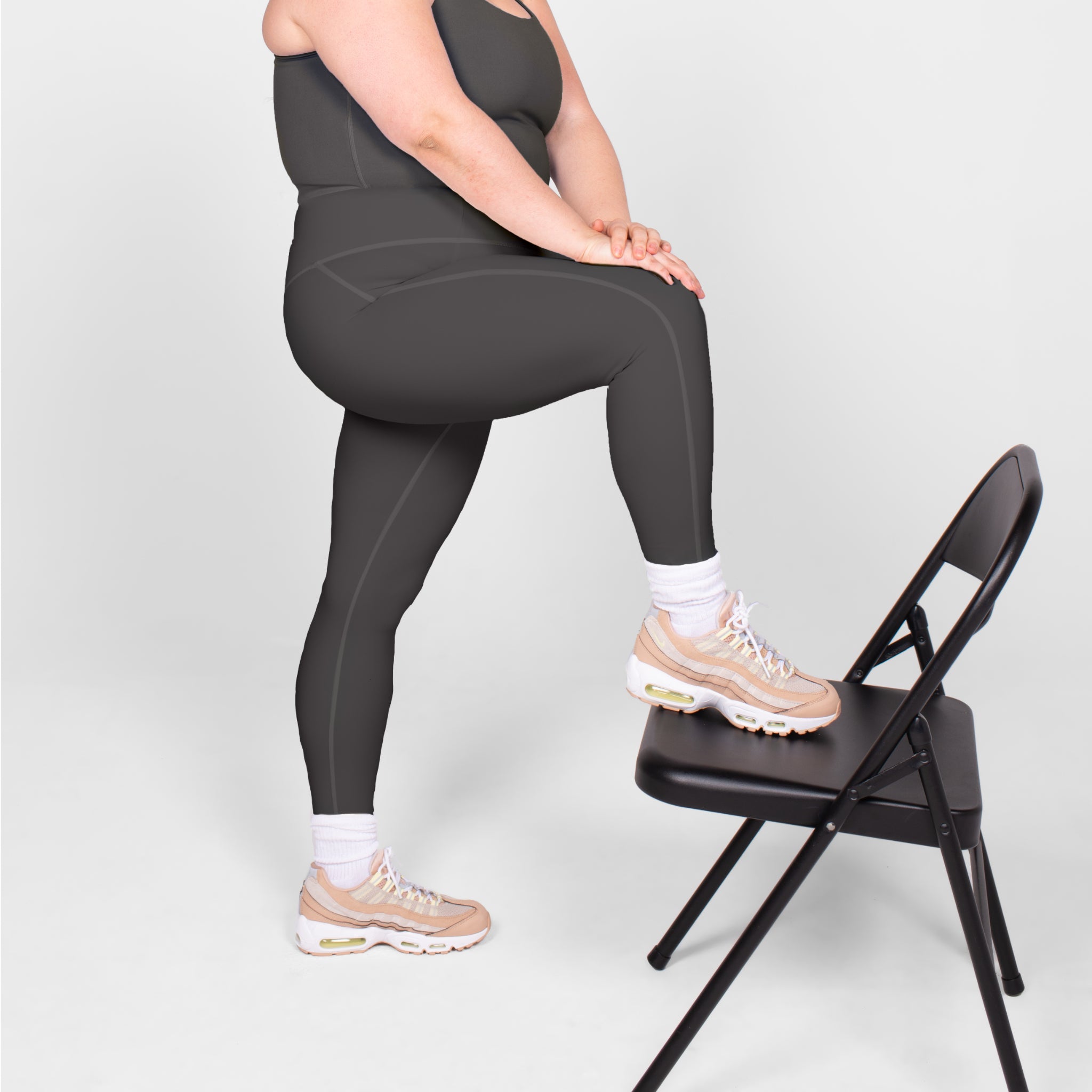 Eine Person in Sportkleidung stützt ihr Bein auf einen schwarzen Klappstuhl.