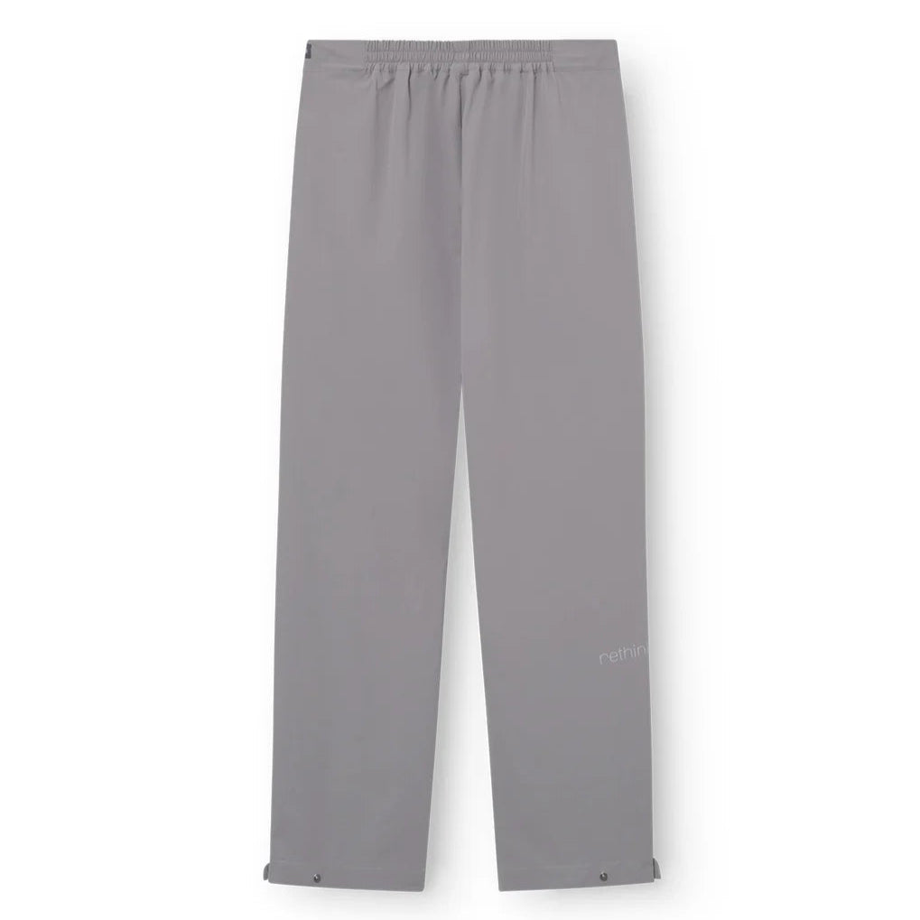 Hellgraue Hose mit geradem Bein, elastischem Bund und verstellbaren Schnappverschlüssen an den Knöcheln, flach auf weißem Hintergrund.