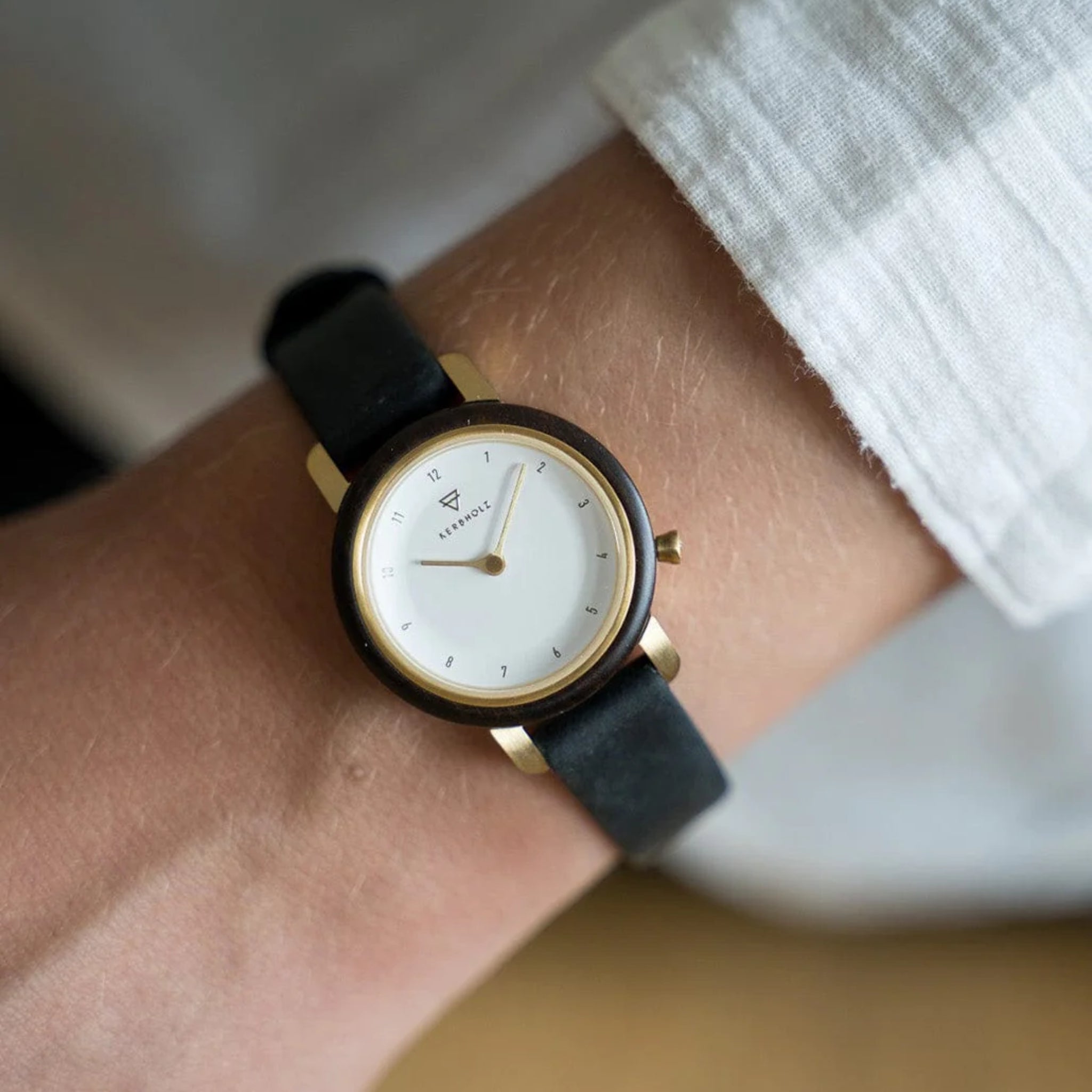Eine elegante Armbanduhr mit schwarzem Lederarmband und rundem Zifferblatt mit goldenen Akzenten an einem Handgelenk.