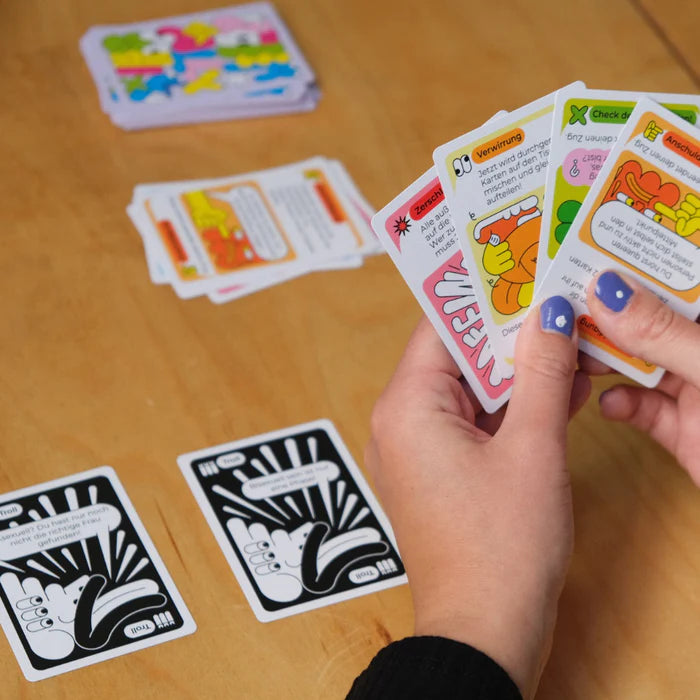 Nahaufnahme von Händen mit bunt illustrierten Spielkarten, die über einem Tisch gehalten werden.