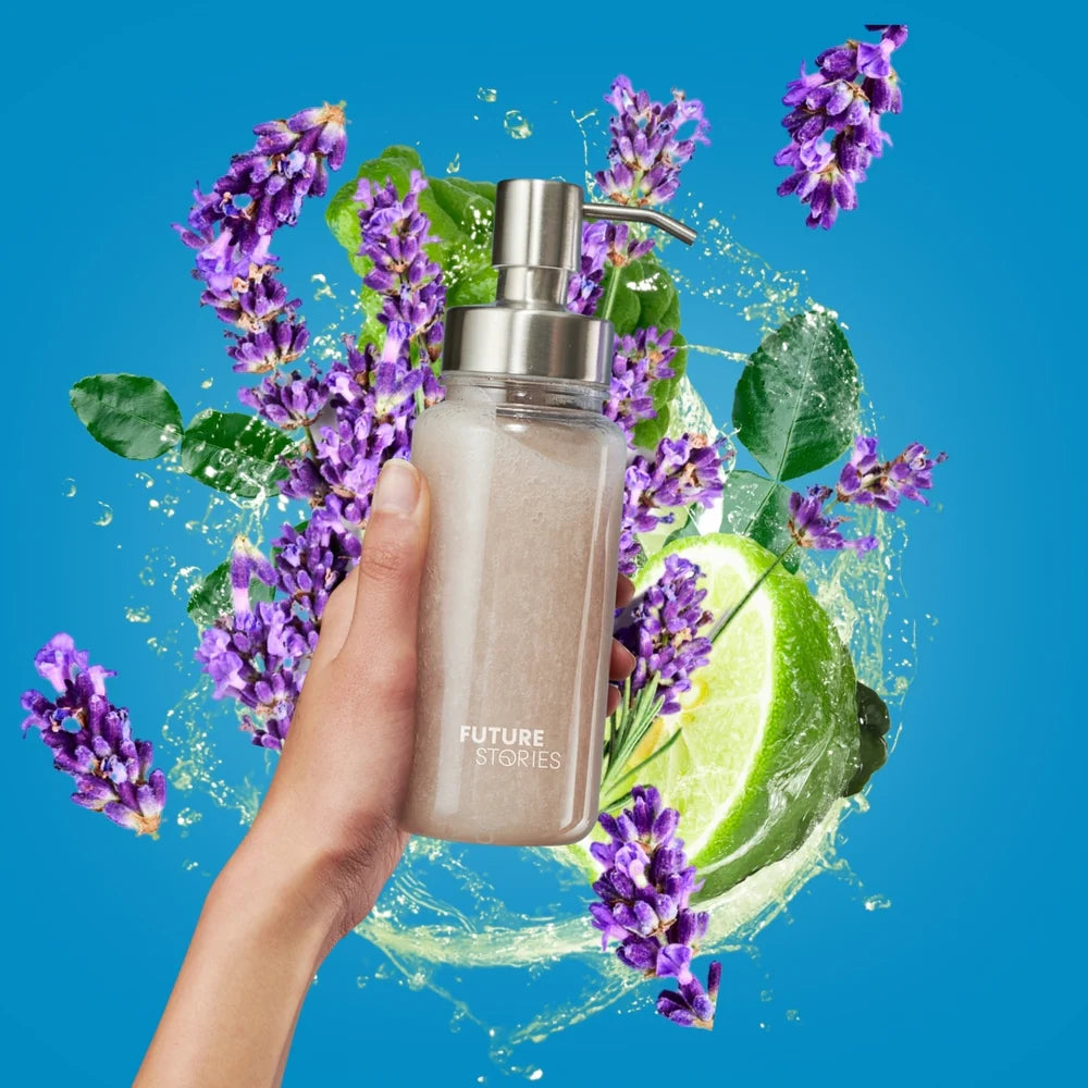Eine Hand hält einen Seifenspender mit der Aufschrift FUTURE STORIES vor einem farbenfrohen Hintergrund mit Lavendelblüten, Limettenscheiben, grünen Blättern und Wasserspritzern auf einem hellblauen Hintergrund.