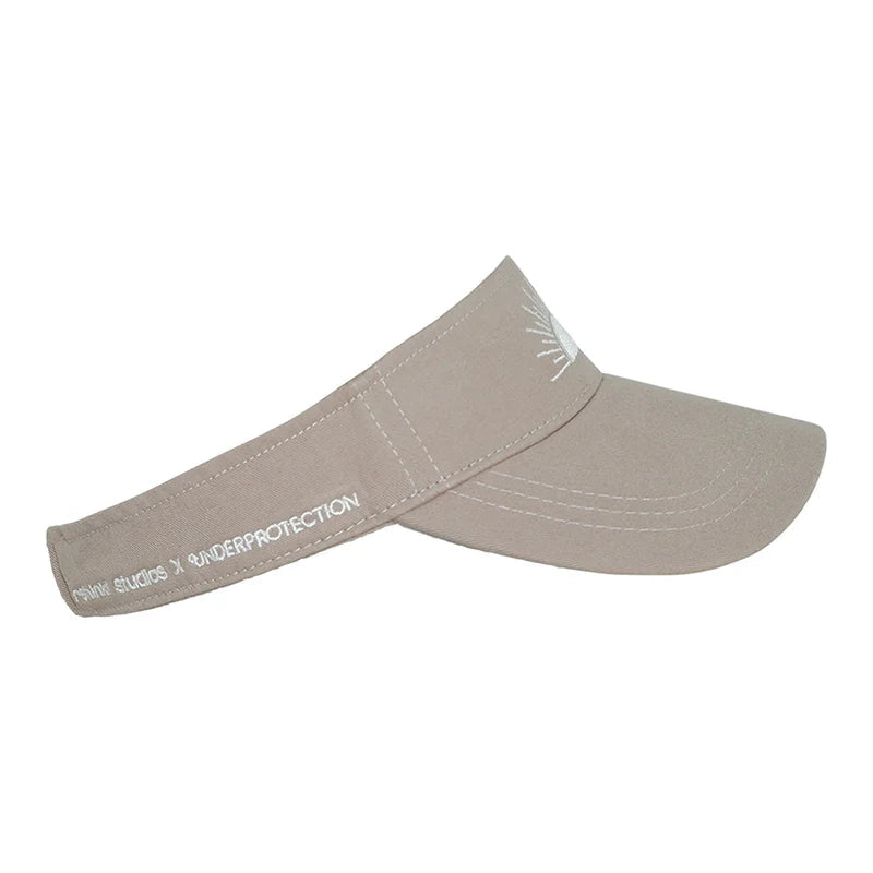 Eine beigefarbene Sonnenblende mit geschwungener Krempe und weißem, gesticktem Text auf der Seite mit der Aufschrift SUN BUMS X UNDERPROTECTION. Auf der Vorderseite befindet sich eine kleine weiße Grafik.