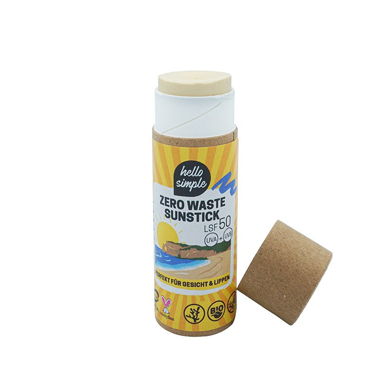 Eine Pappröhre mit der Aufschrift Zero Waste Sunstick SPF 50 steht aufrecht, der Deckel ist zur Seite gelegt. Die Verpackung ist umweltfreundlich und zeigt gelbe, blaue und grüne Grafiken mit Bildern von Sonnenlicht und Natur.