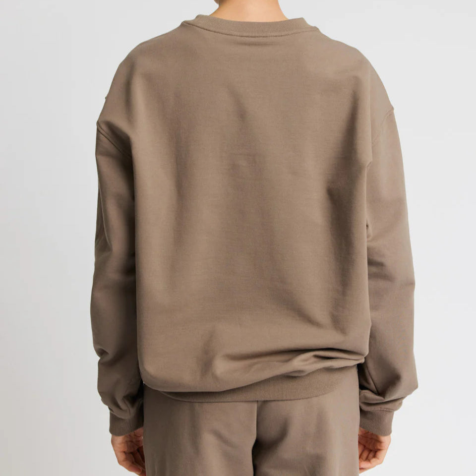 Person in braunem Sweatshirt und passender Hose von hinten betrachtet.