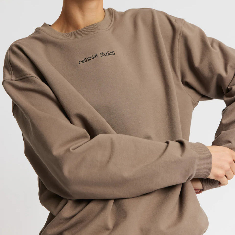 Person in einem beigen Sweatshirt mit dem Aufdruck "rethinkit studios" auf der Vorderseite.